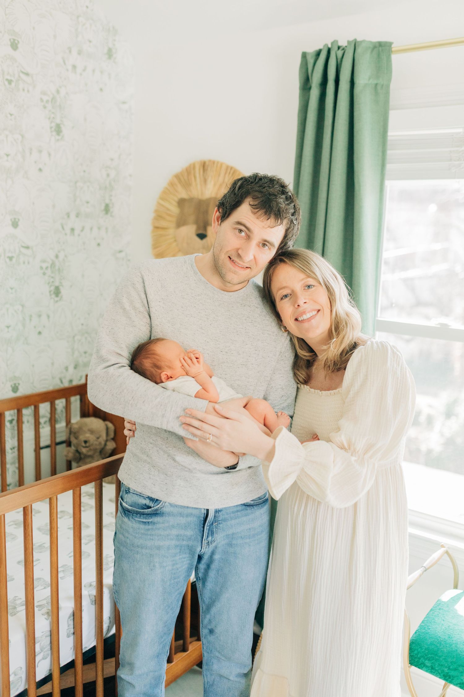 Parents share intimate moment while holding newborn baby in front of wooden crib.