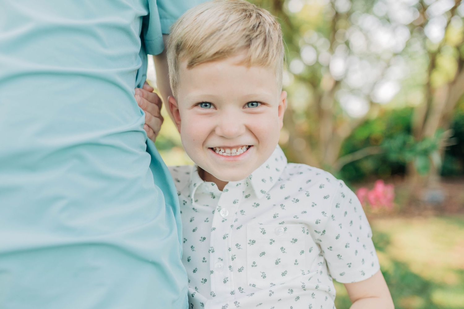 Family portrait session in a garden setting with blooming pink flowers and natural sunlight.