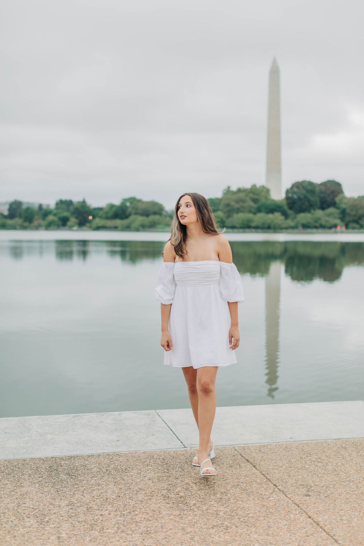 White off-shoulder dress photo at the Washington Monument reflecting pool on an overcast day.