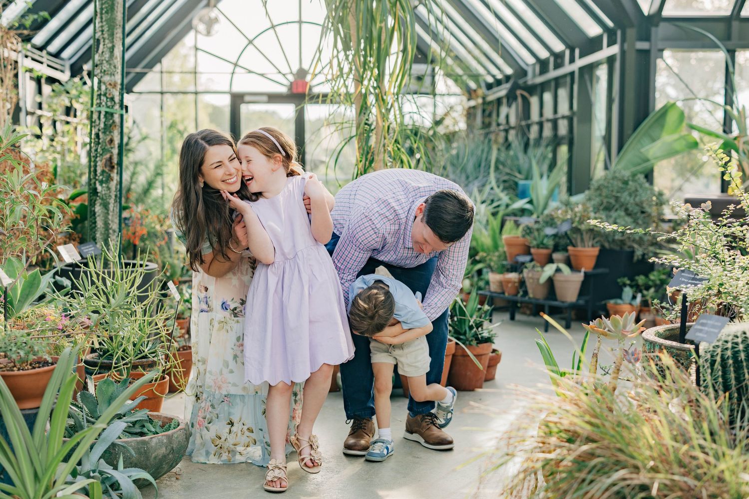 Family sharing a tender moment in a lush greenhouse surrounded by tropical plants and cacti.