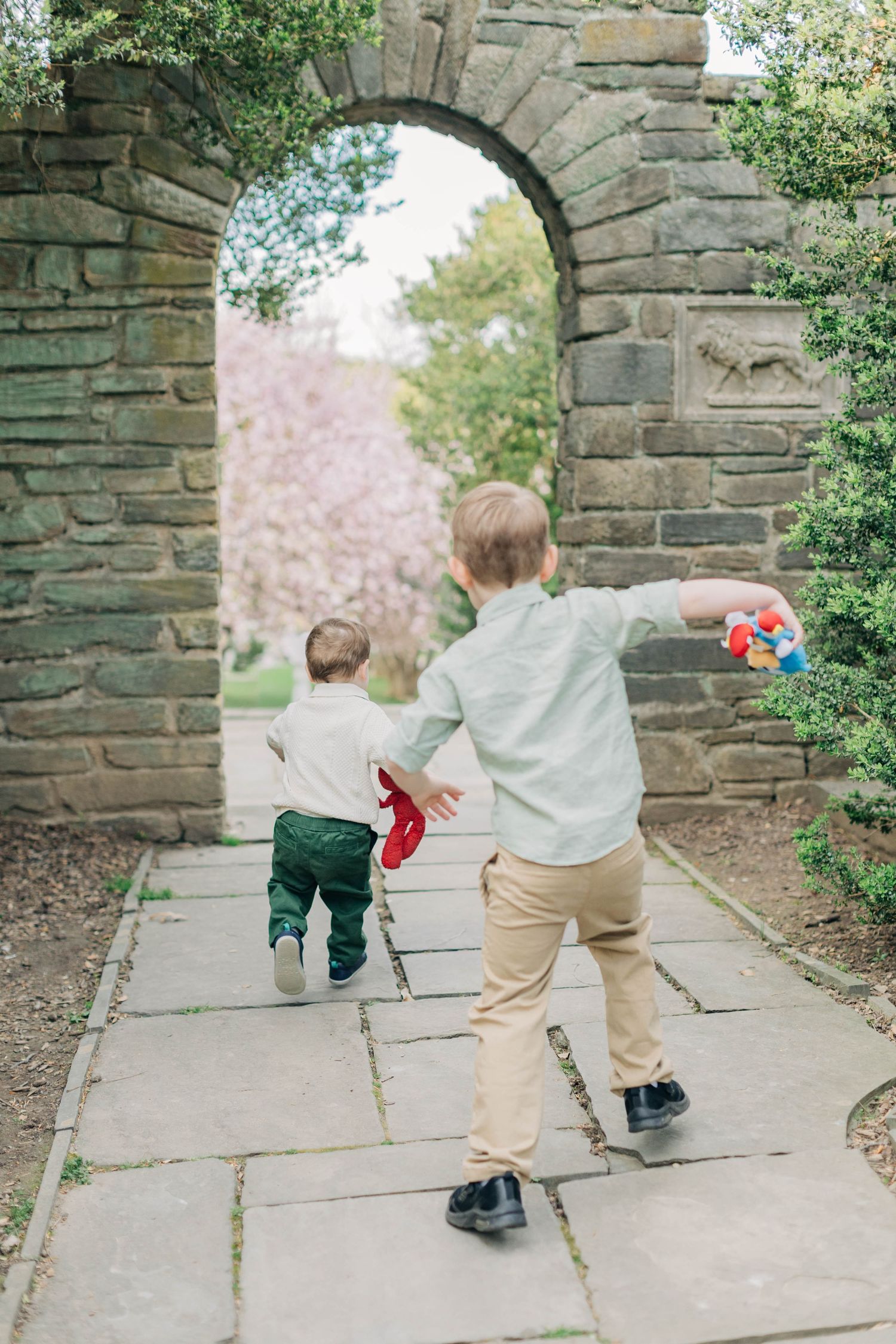 Two young boys walking through a stone archway in a garden with cherry blossom trees in spring.