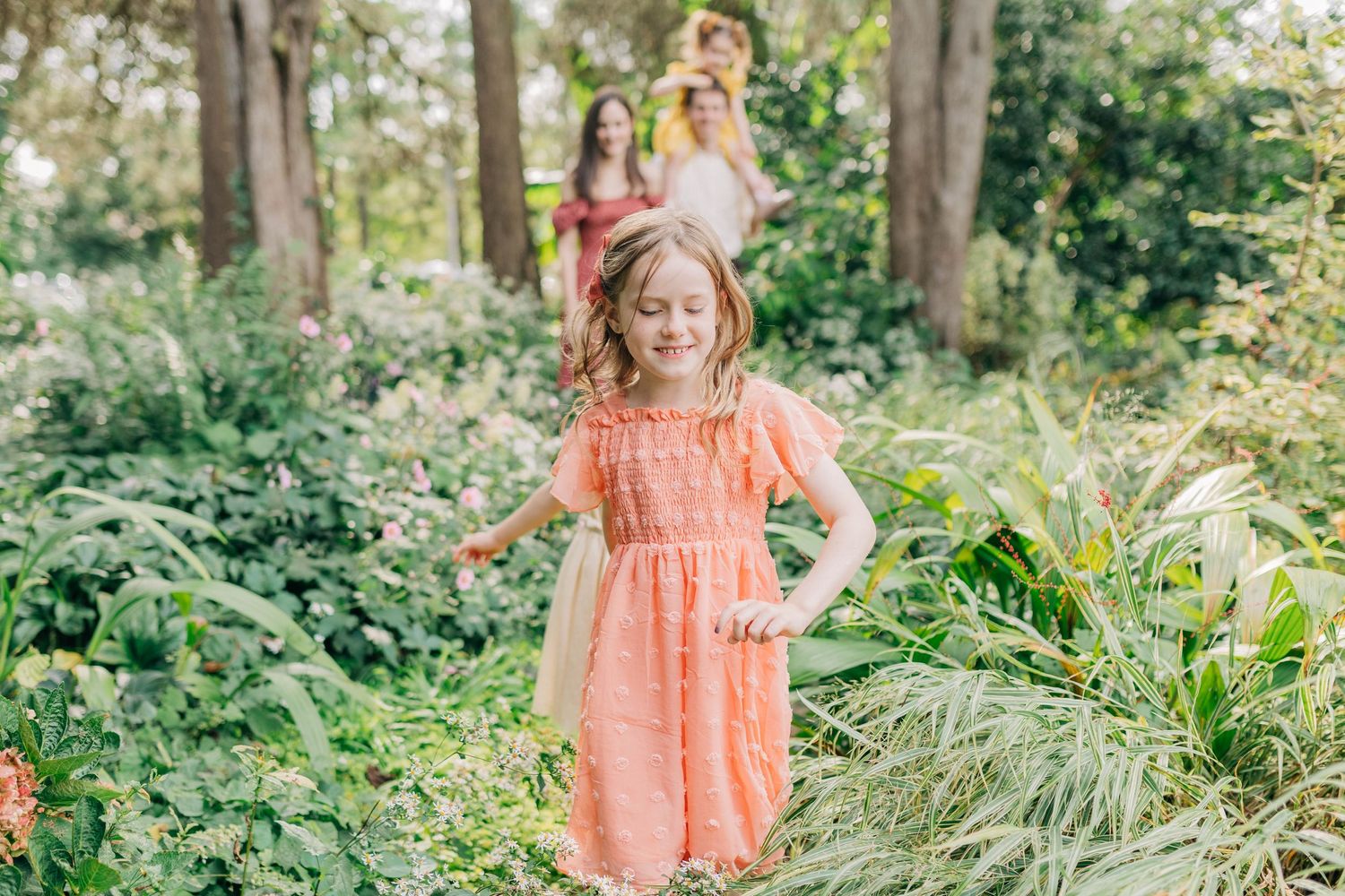 A whimsical summer photoshoot in a lush garden with coral dresses and natural greenery.