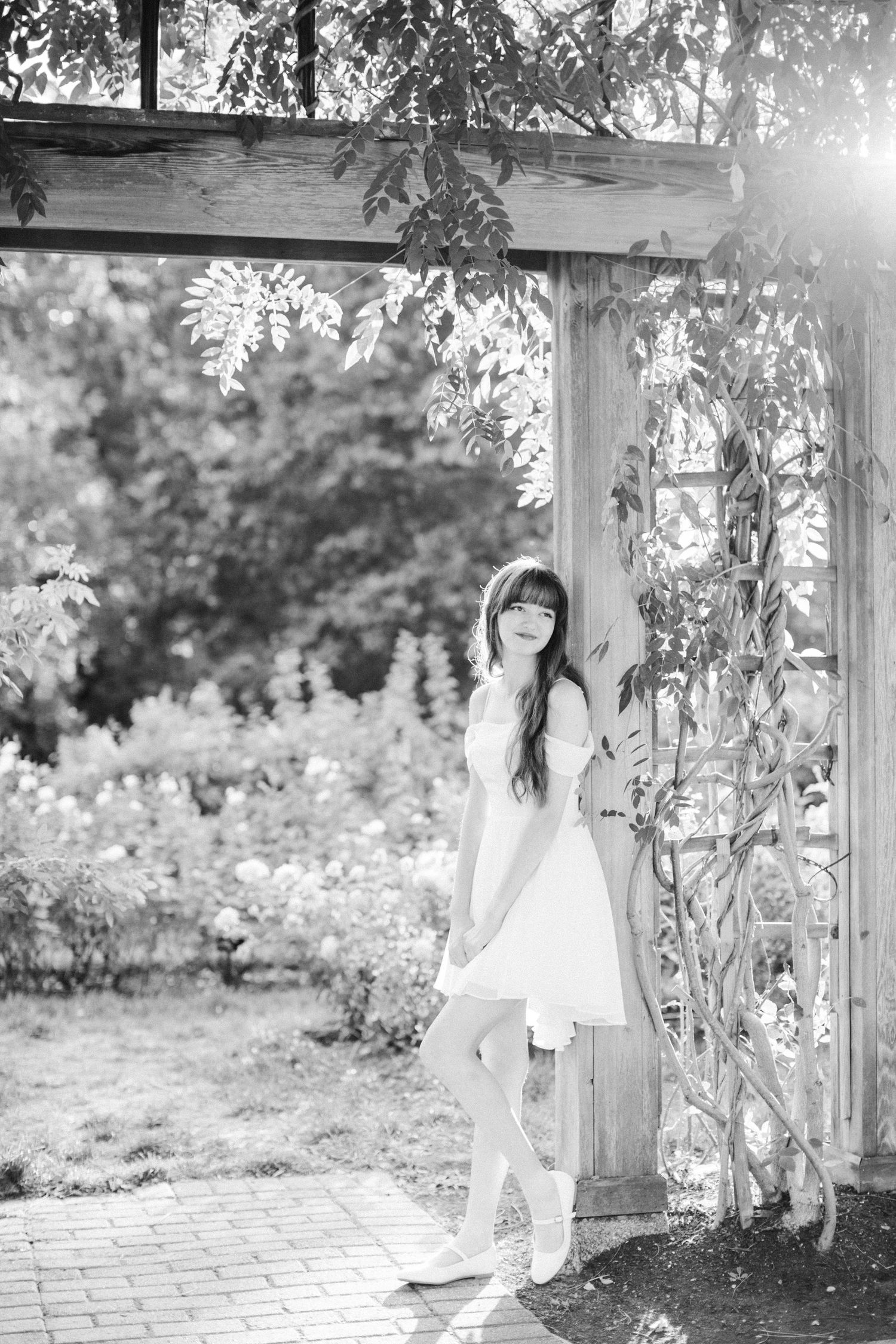 Black and white portrait in a garden pergola with dramatic lighting and natural elements.