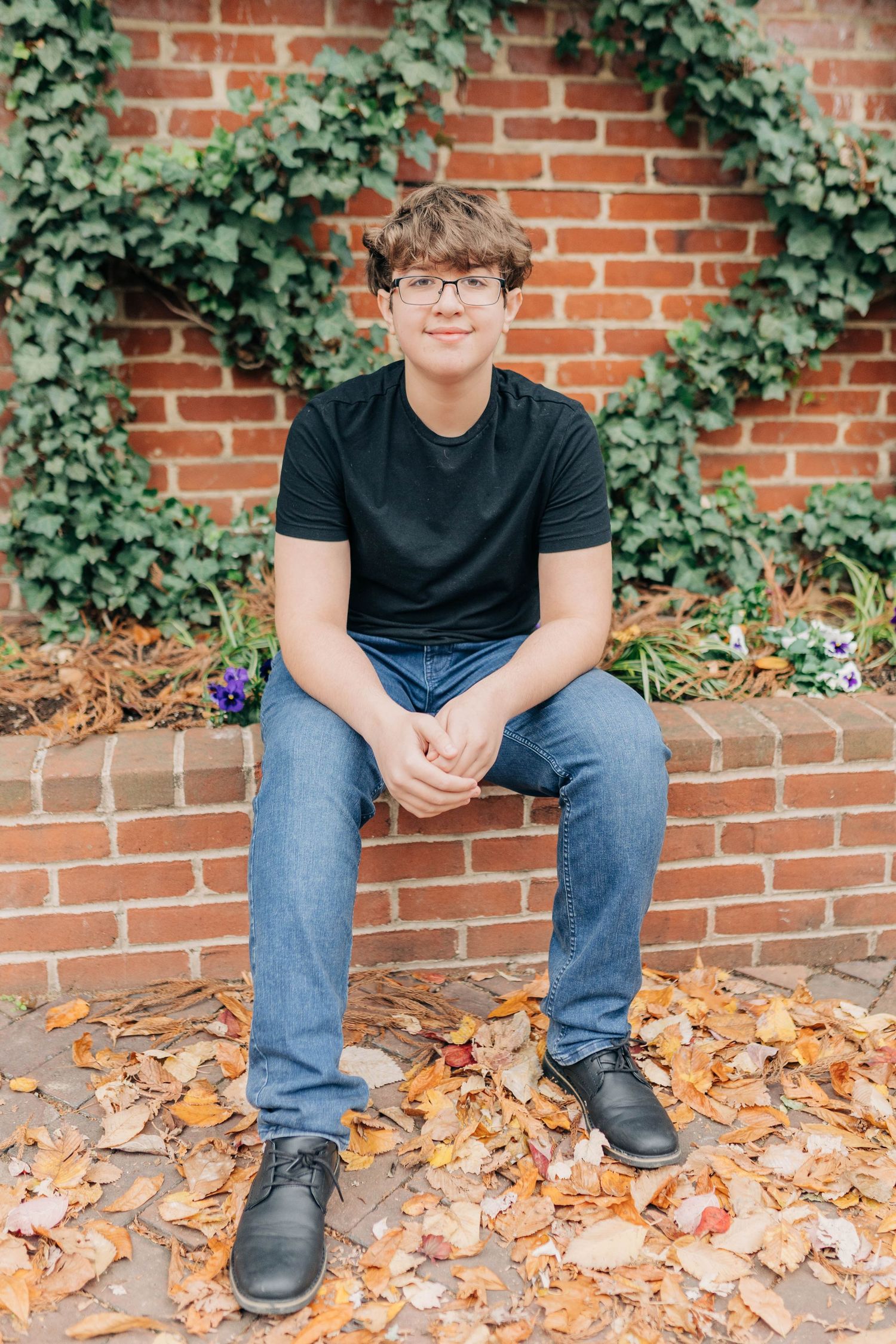 Casual portrait session featuring autumn leaves and brick wall backdrop.