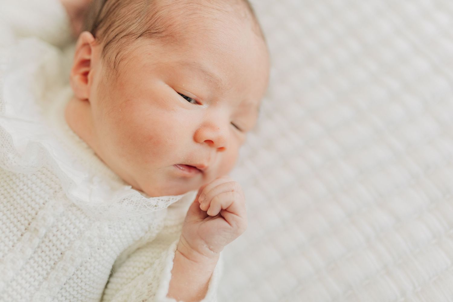 Sleeping infant in white knit clothing on textured white background.
