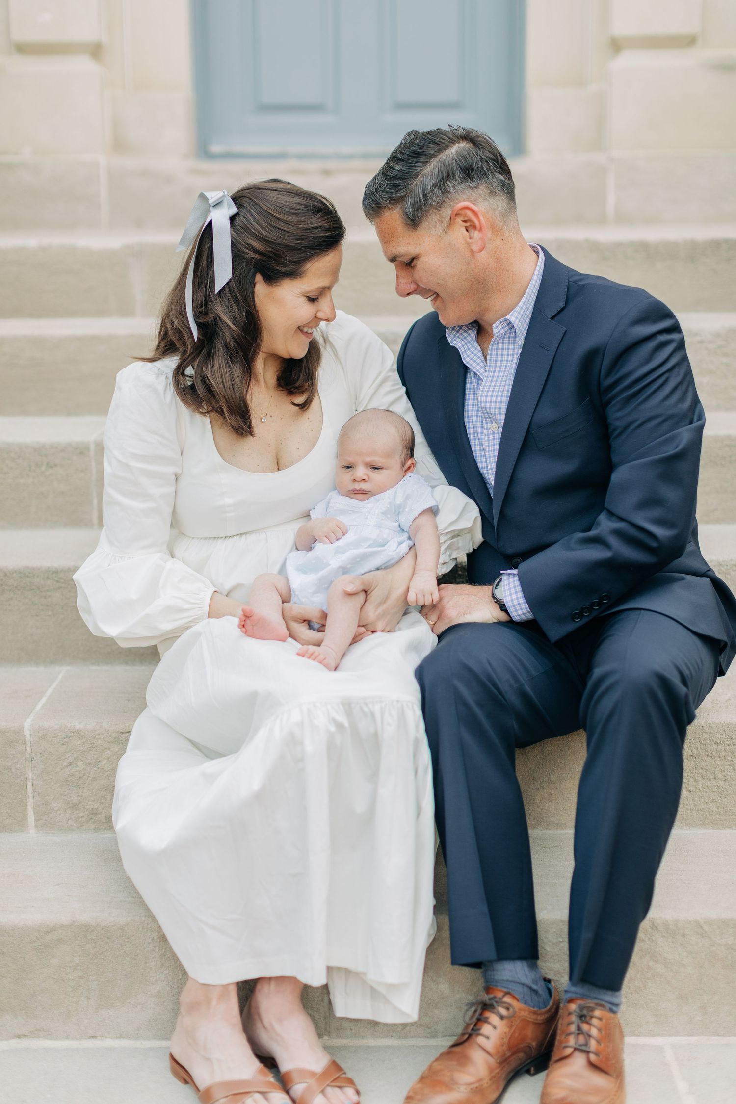 A family of three sits together on concrete steps outside a building.