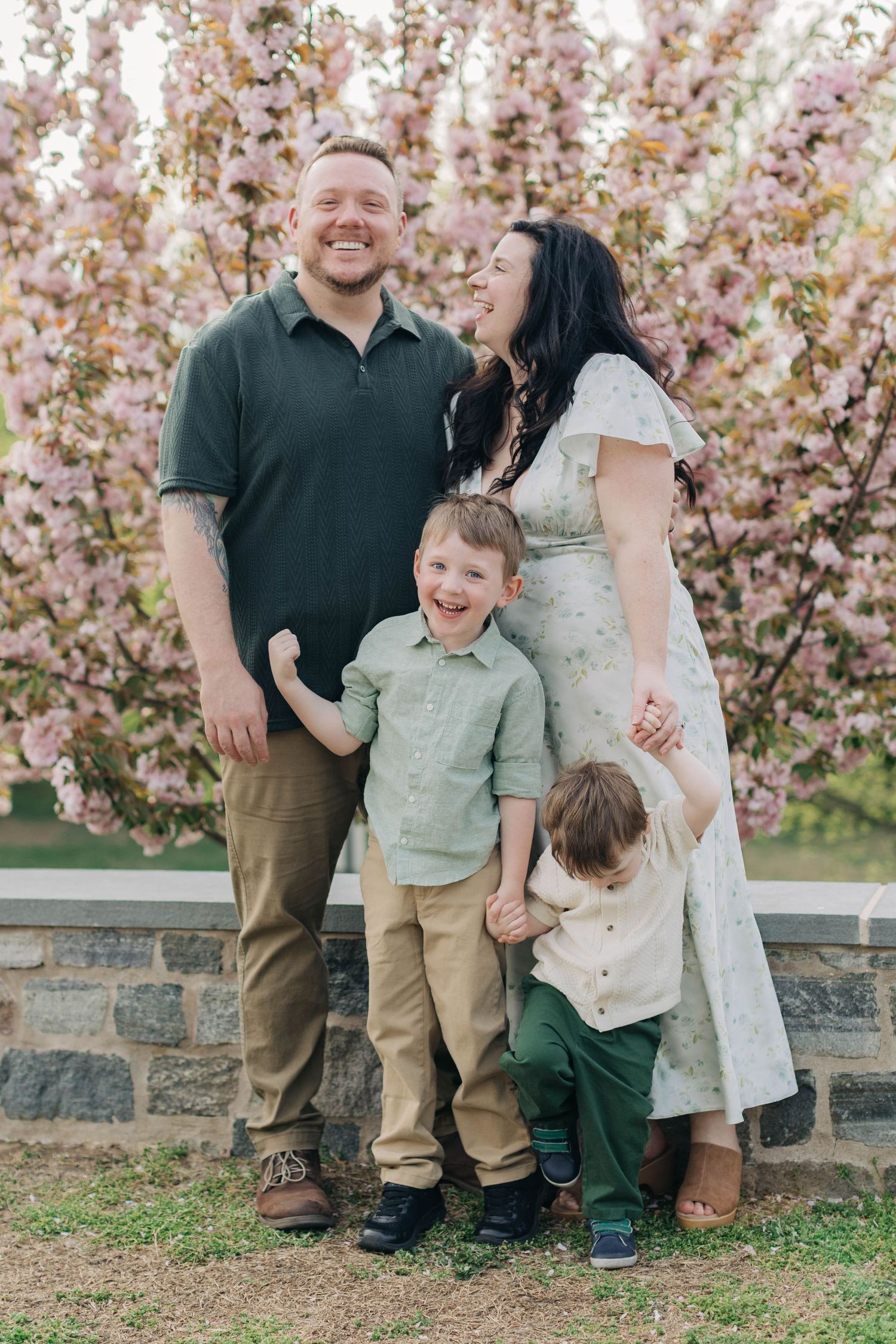 Happy family of four posing outdoors near pink cherry blossom trees in spring.
