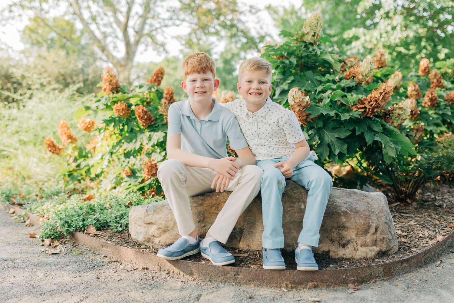 Family members sitting on stone garden edging during outdoor photo session.