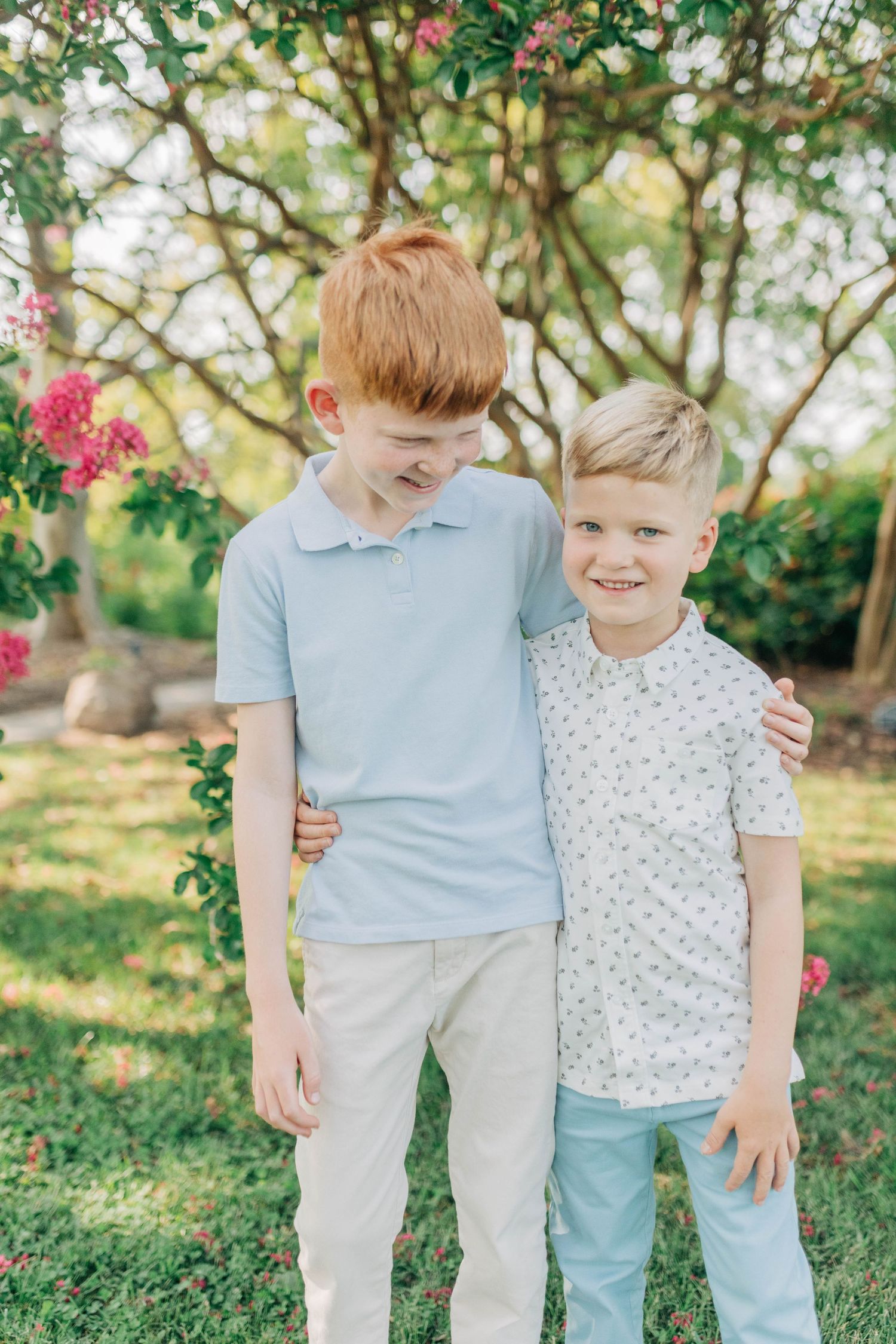 Two children in light blue and white outfits posing together in a flowering garden.