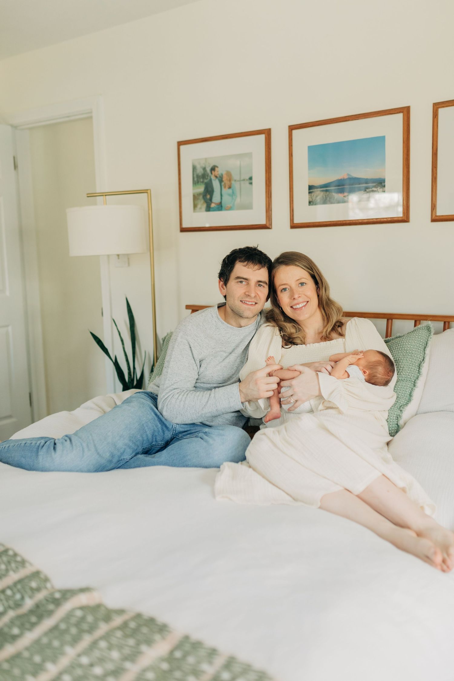 Relaxed family portrait on bed with coastal artwork displayed on wall.