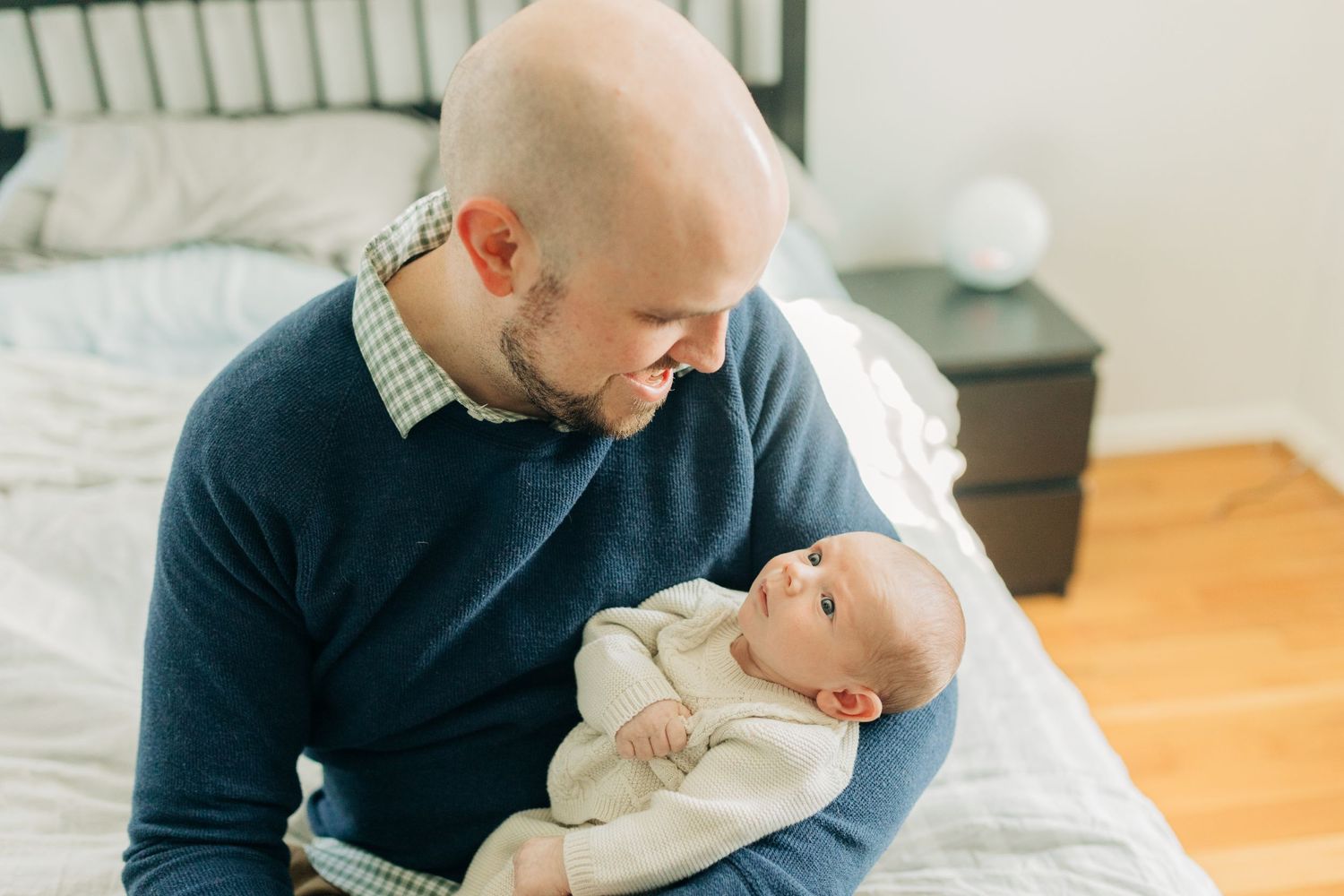 Close-up shots of parent cradling infant in navy sweater against bright interior.