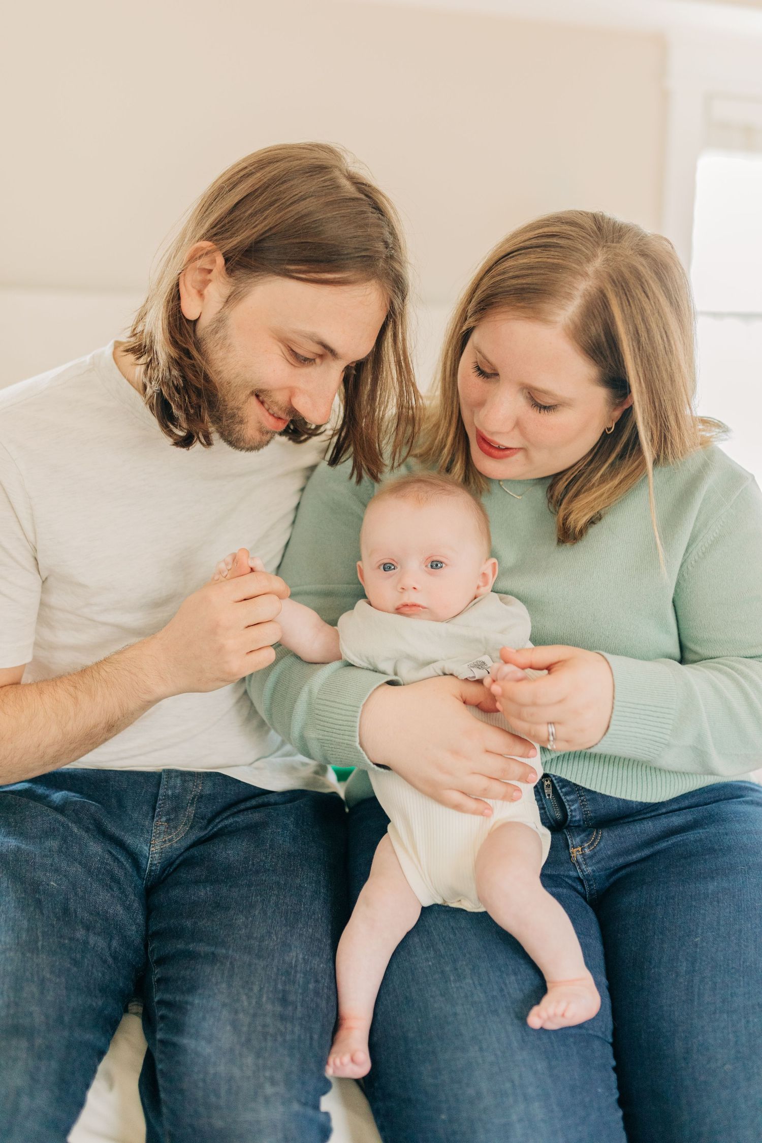 Intimate family portrait with baby wearing white onesie on bed.