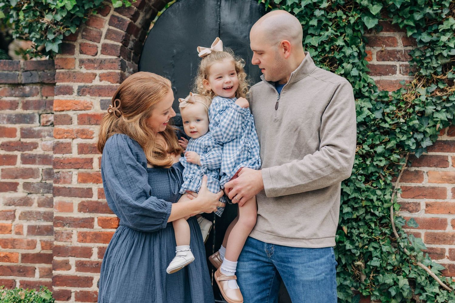 Family poses against brick wall with ivy during outdoor photo session.