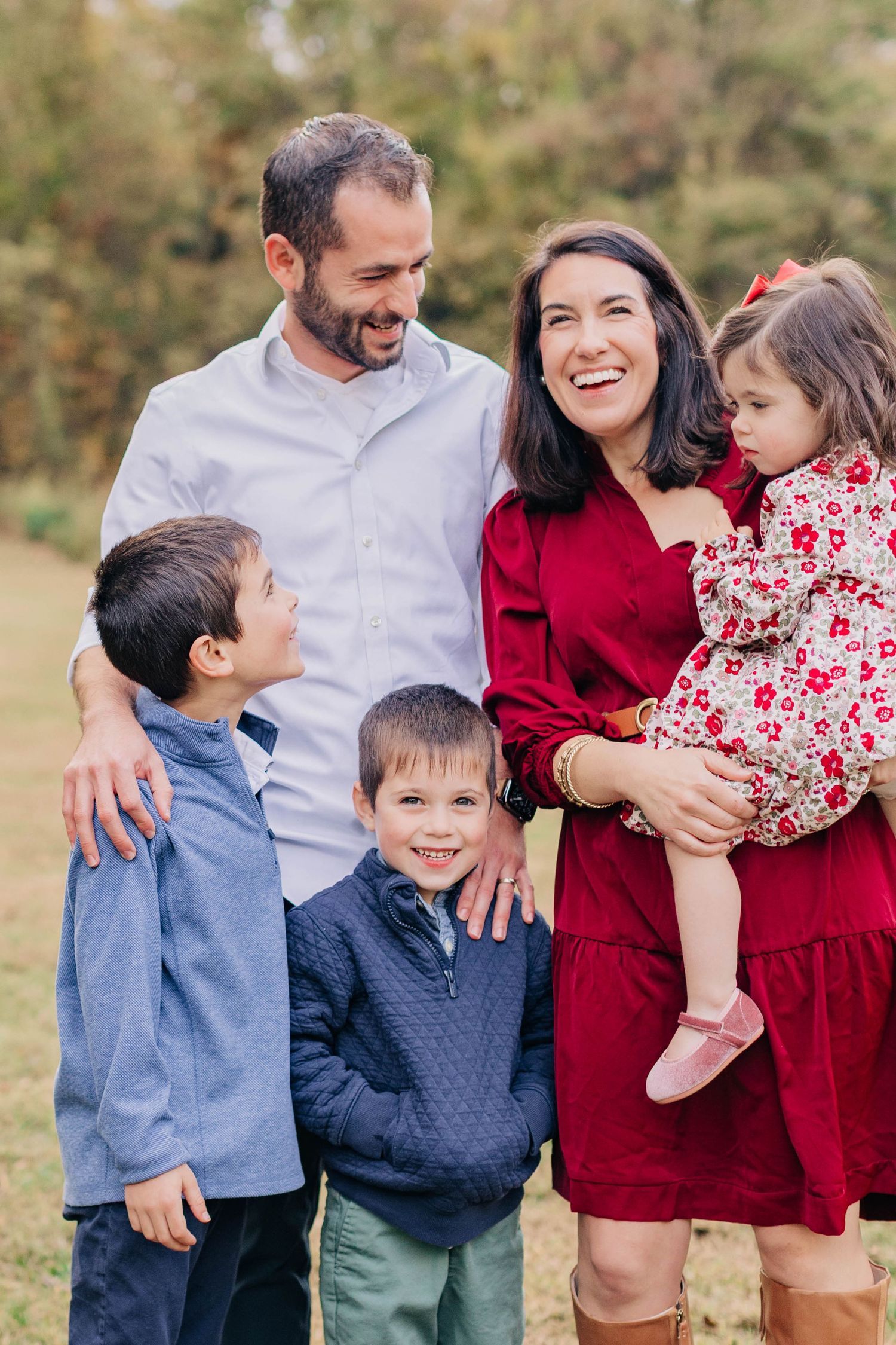 Happy family of five smiling outdoors in fall, parents with three young children dressed in red and blue.