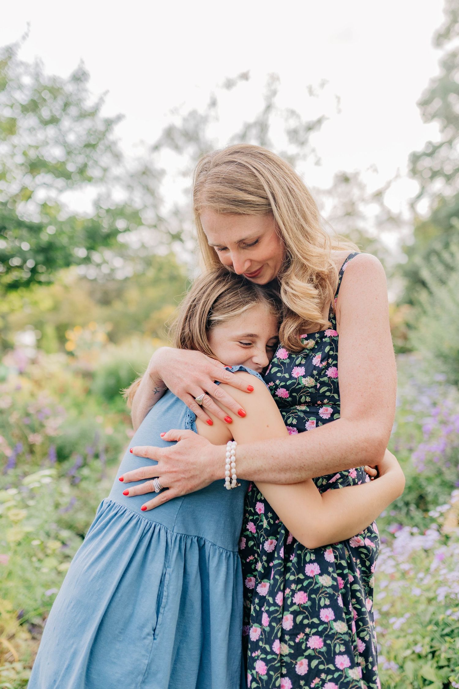 A tender embrace is shared between two people wearing blue and floral dresses in a garden setting.