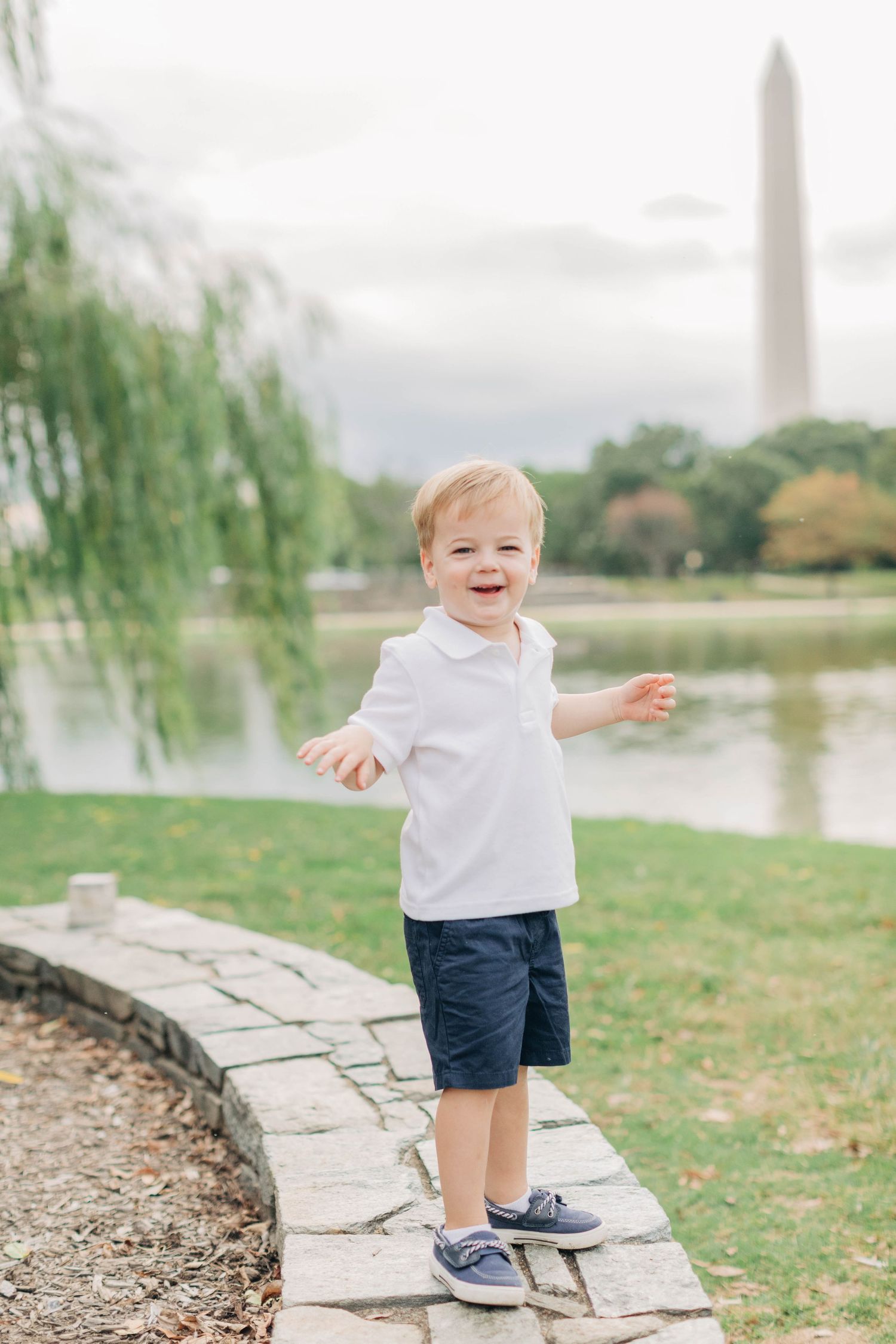 A toddler in white shirt and navy shorts plays near the Washington Monument reflecting pool.