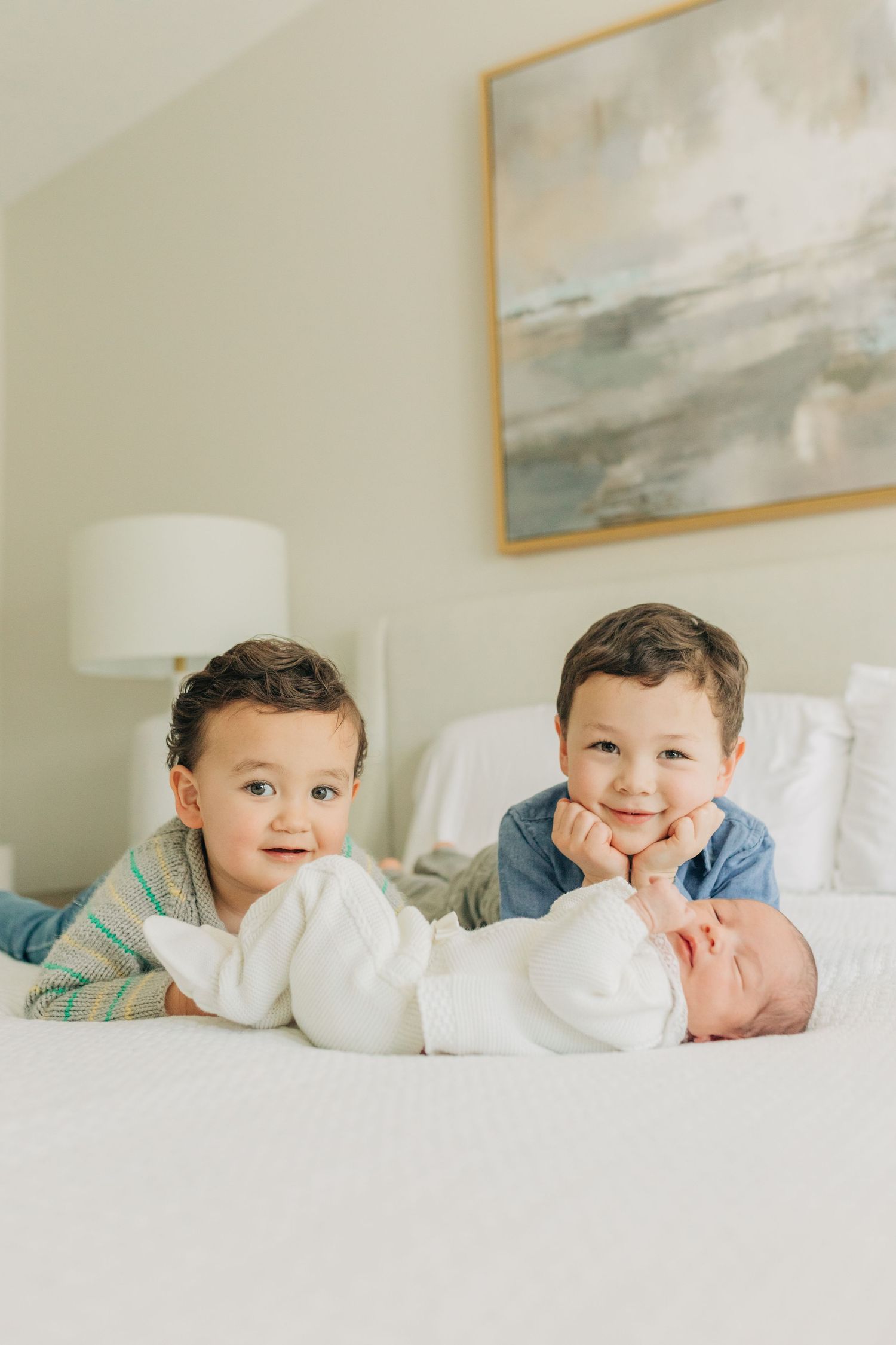 Children lying on a white bed making playful expressions in a bedroom with soft natural lighting.