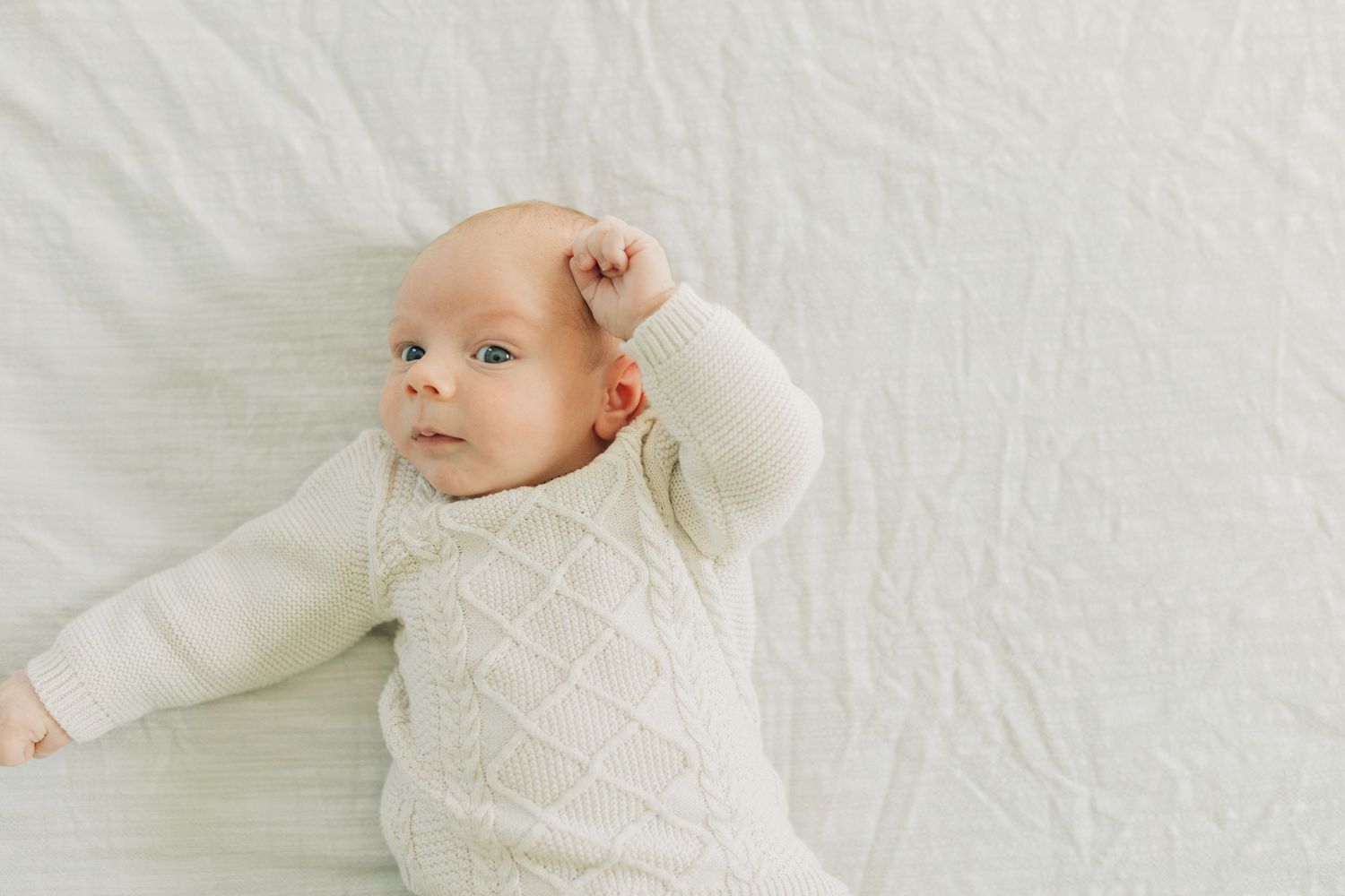 Close up of infant in cream colored sweater on white bedding.