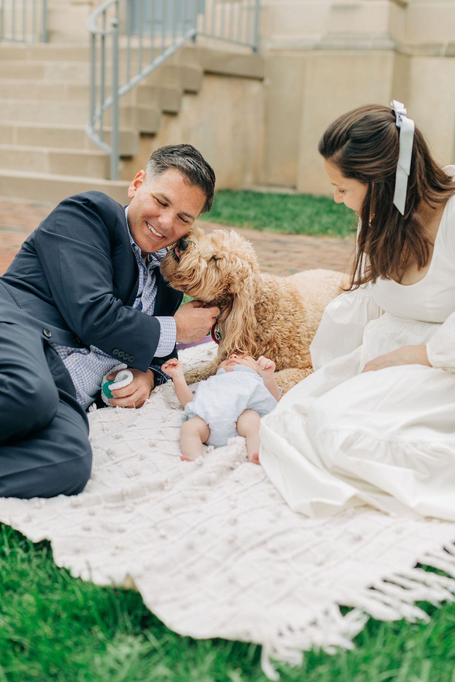 Family relaxes together on white blanket during outdoor photo session.