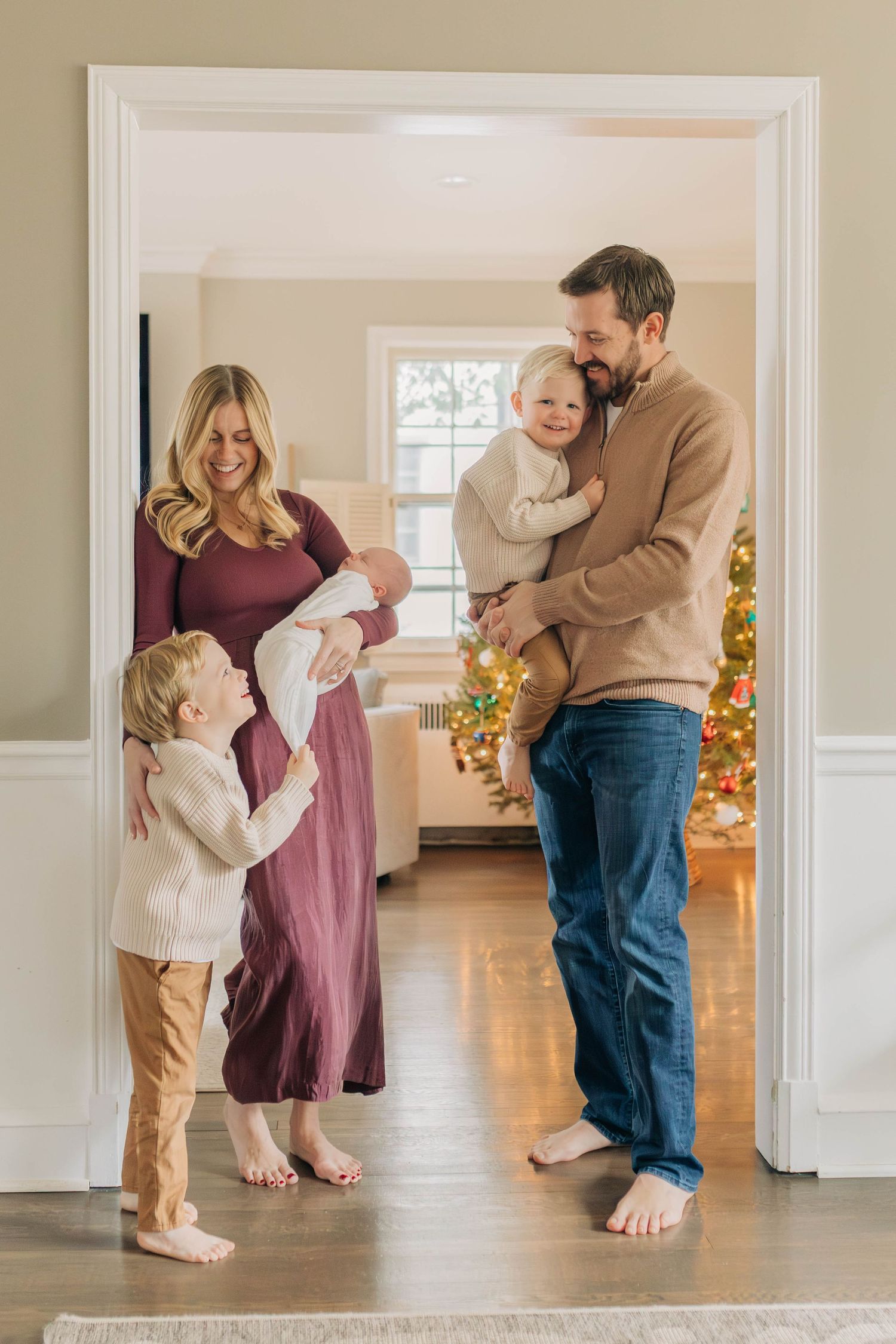 A family stands barefoot in a doorway of their home during a holiday photoshoot.