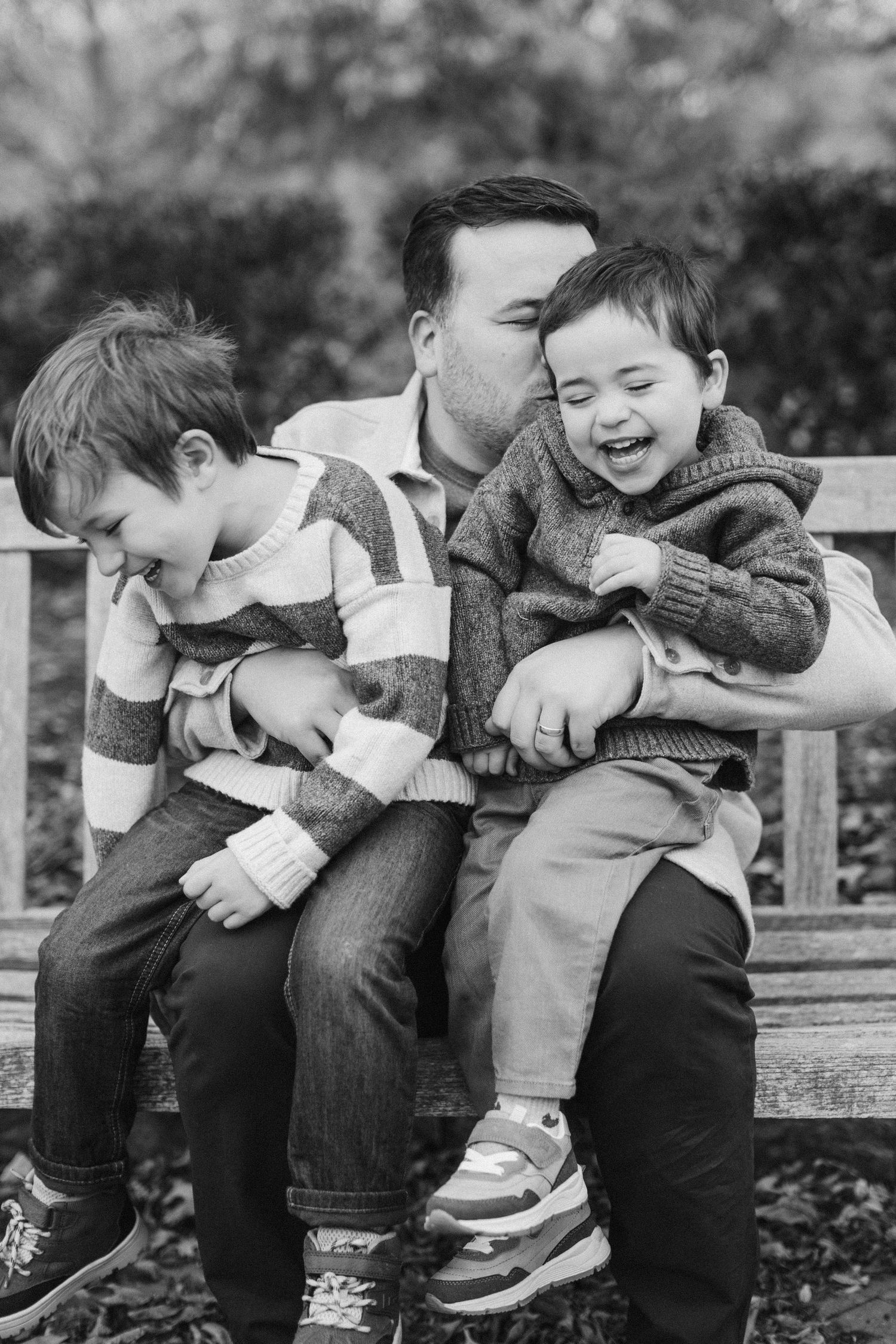Children sitting on a wooden bench sharing playful moments in black and white.