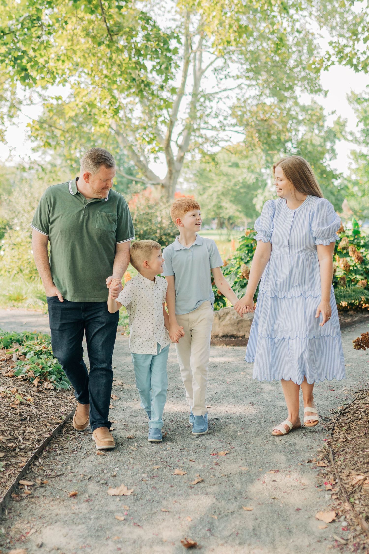 Family walking together on dirt path surrounded by green trees and plants.
