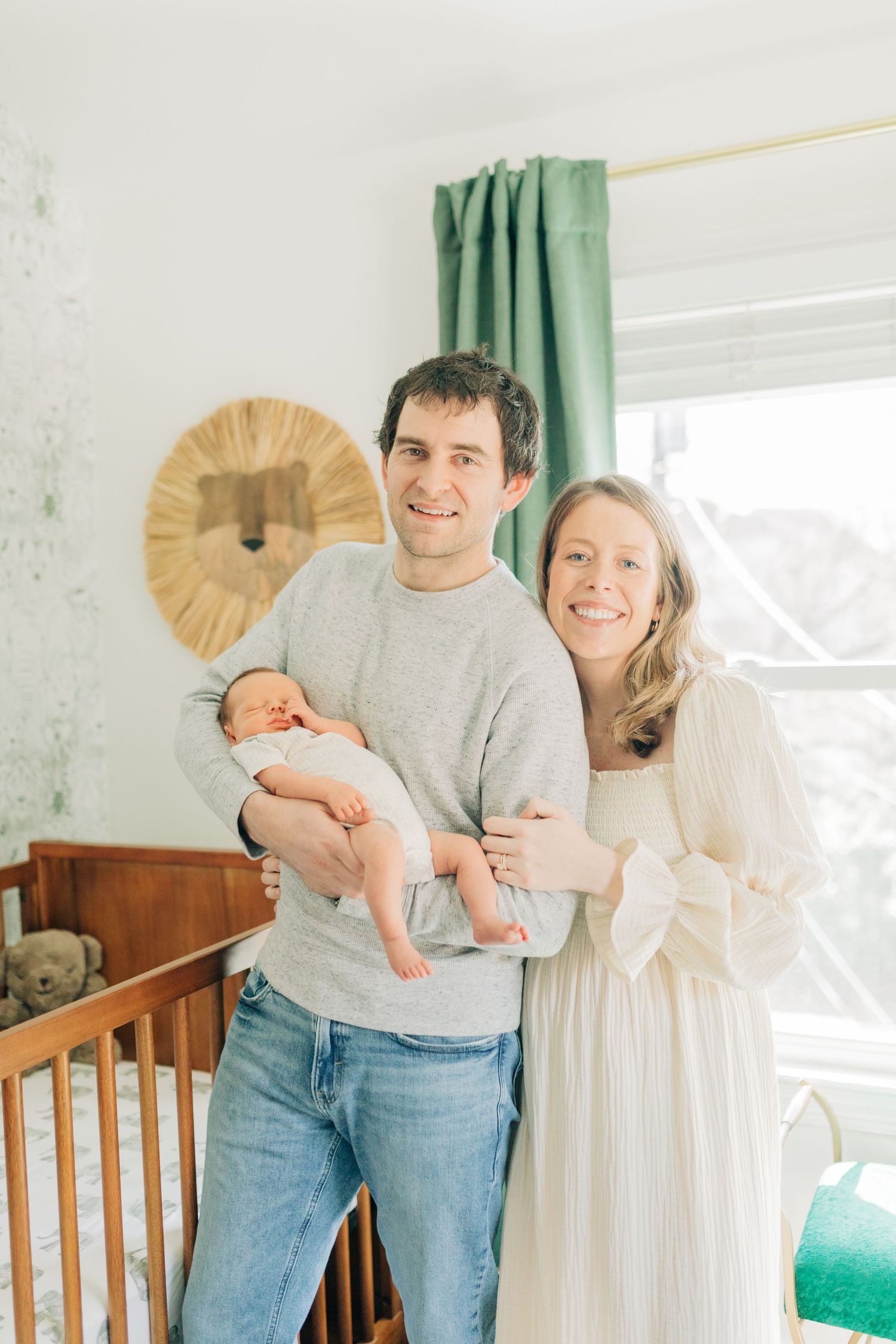 Parents pose with newborn baby in nursery decorated with wooden crib and lion wall art.