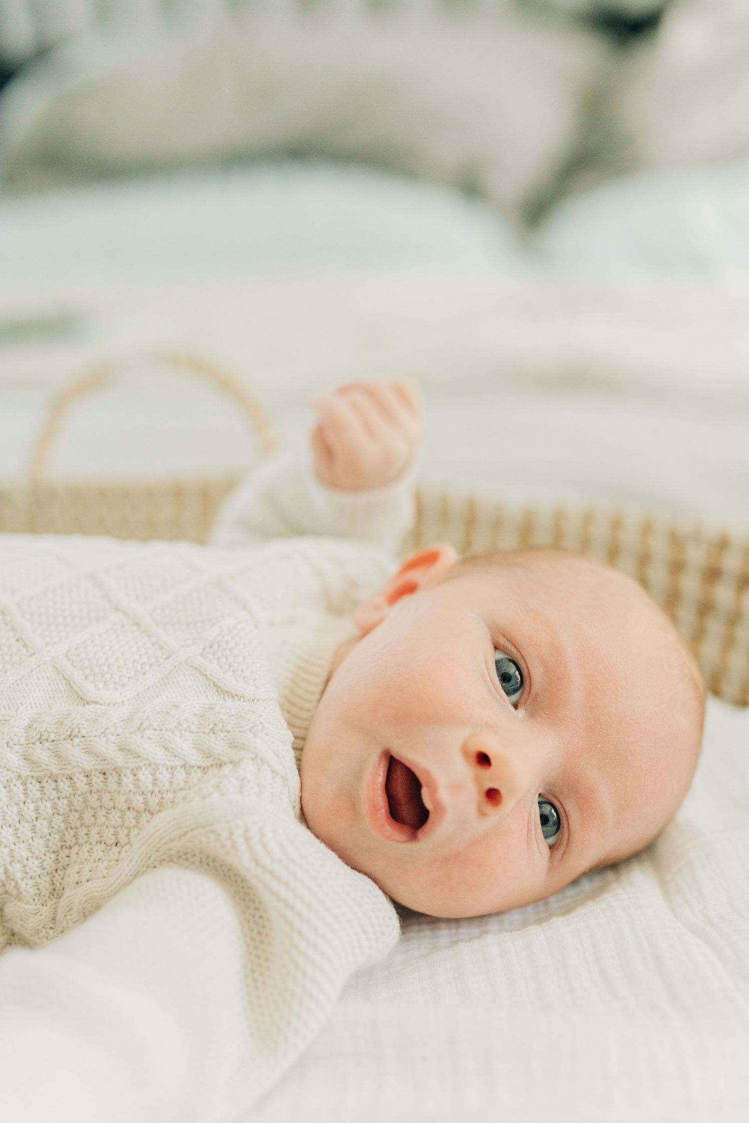 Adorable baby in white knit sweater lying on textured surface with expressive face.