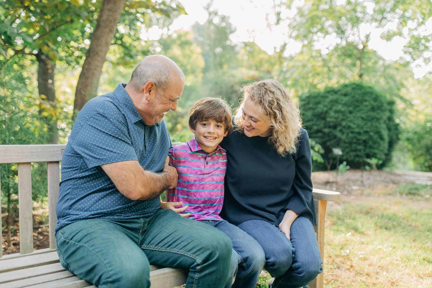 Family members share laughs while sitting together on wooden bench in garden setting.