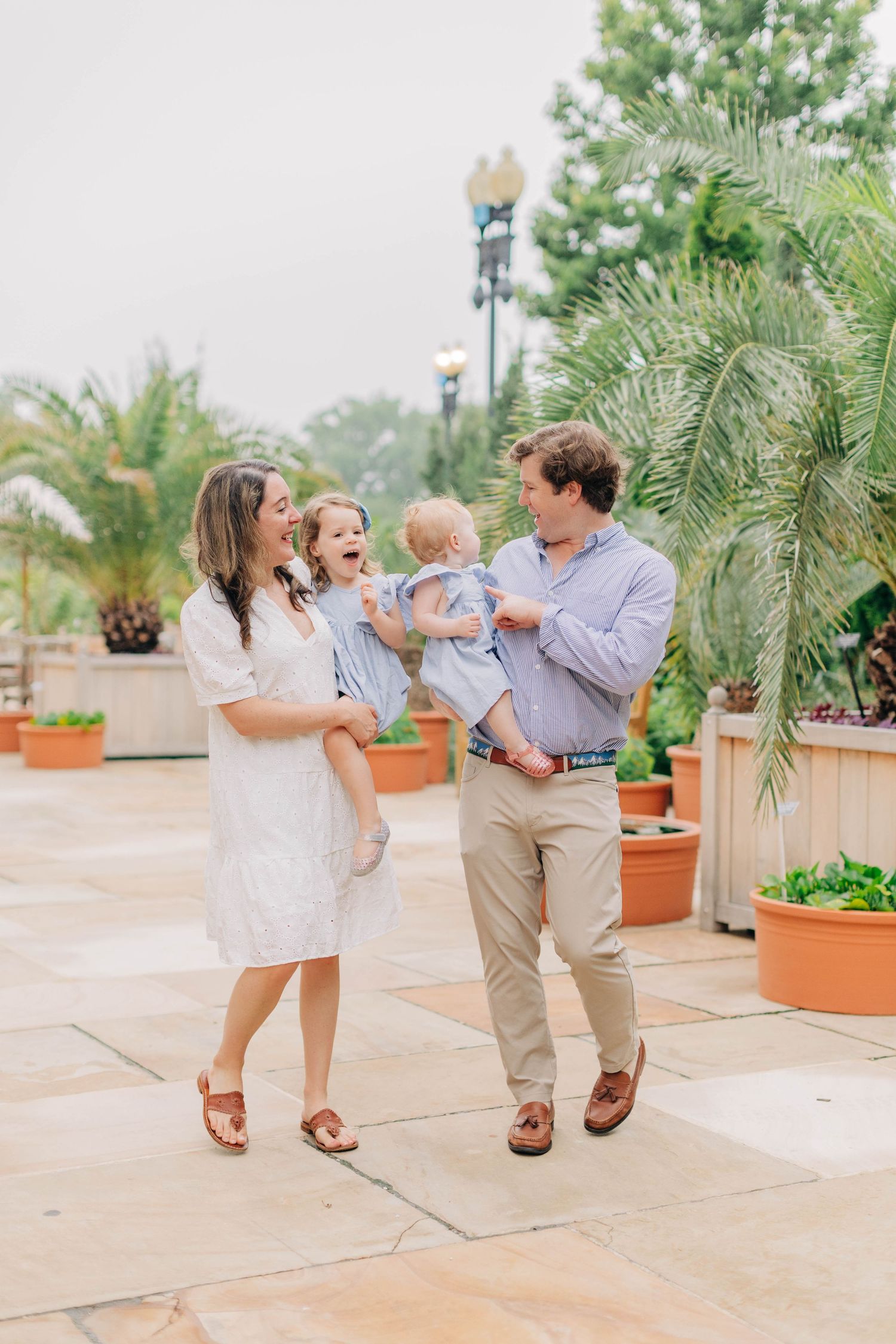 Happy family with two young children laughing together on a stone patio surrounded by tropical plants.