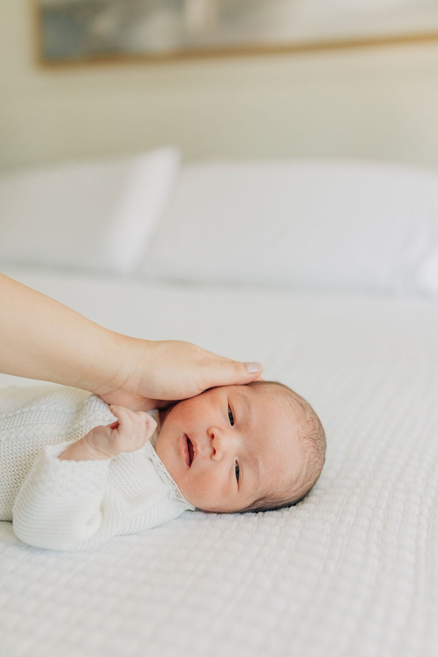 Gentle hand touching sleeping baby's head on white textured bedding.