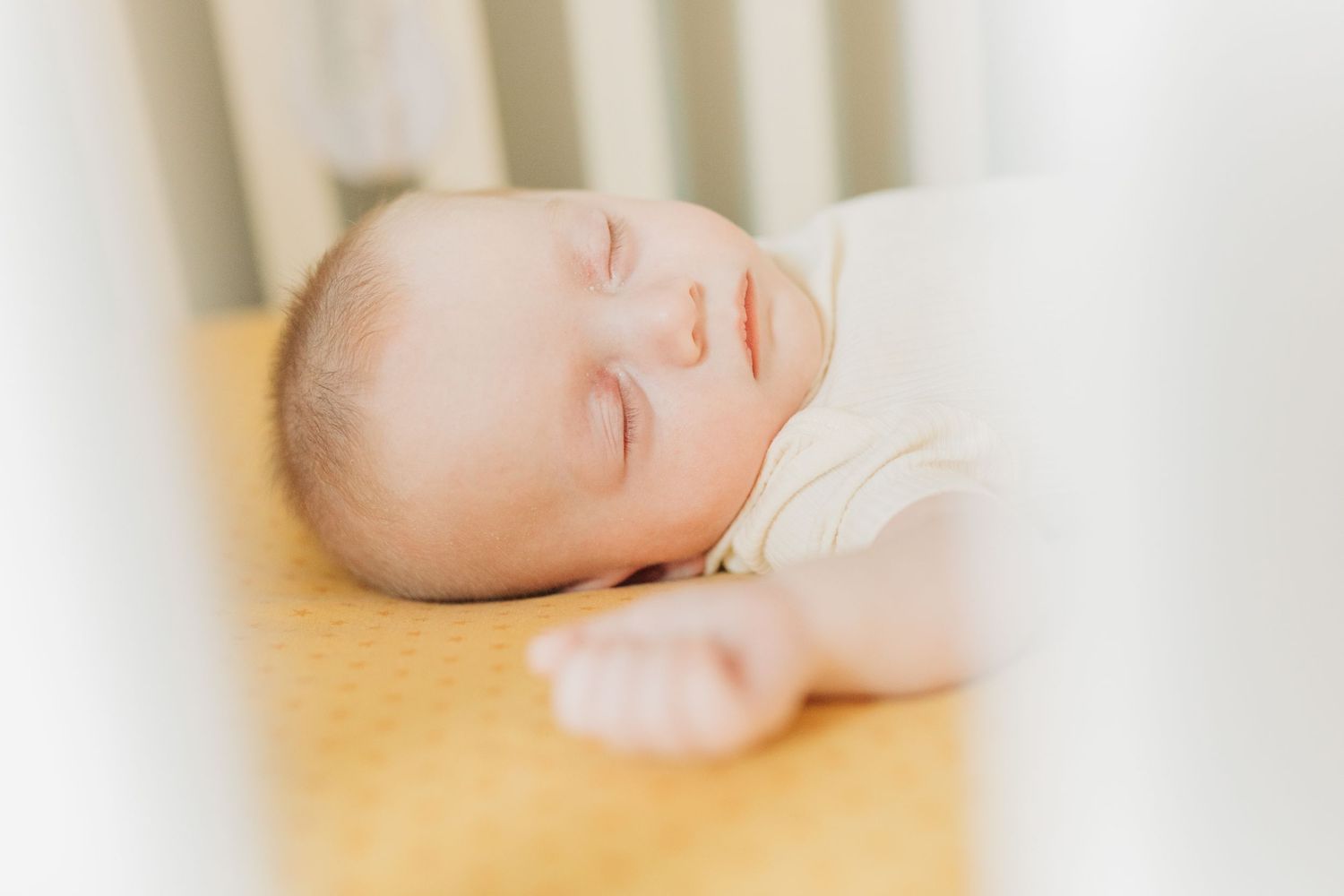 Baby in white onesie lying peacefully on white bedding.