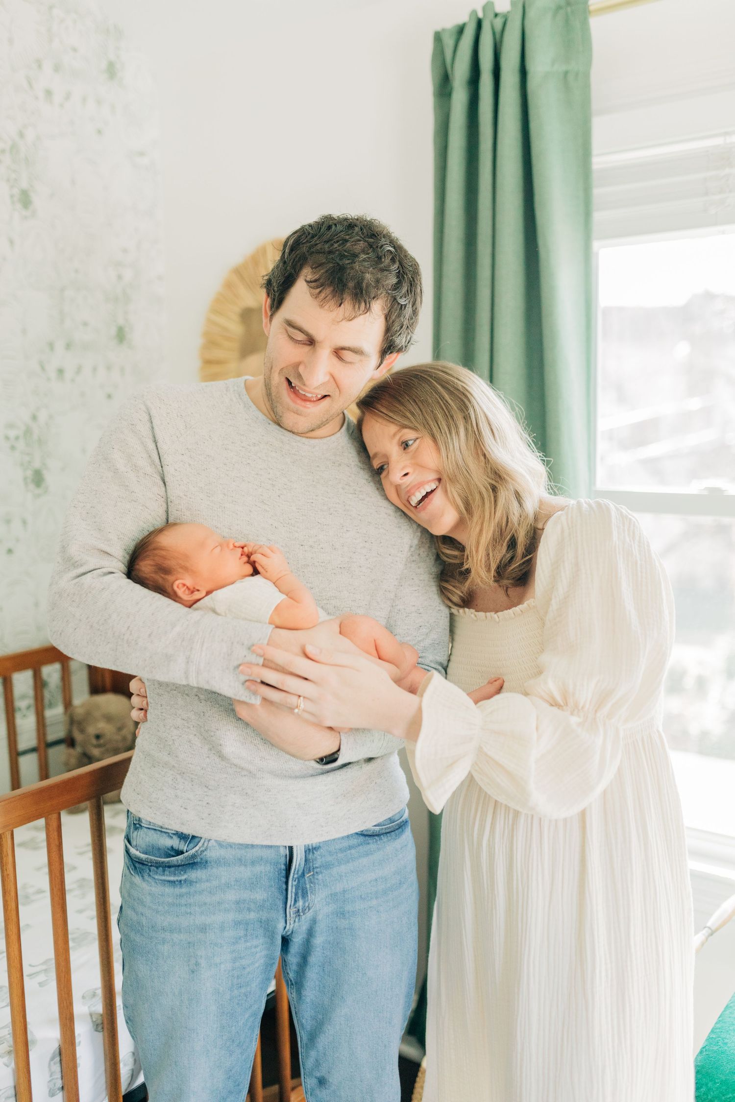 Parents share joyful moment while cradling newborn baby in nursery setting.