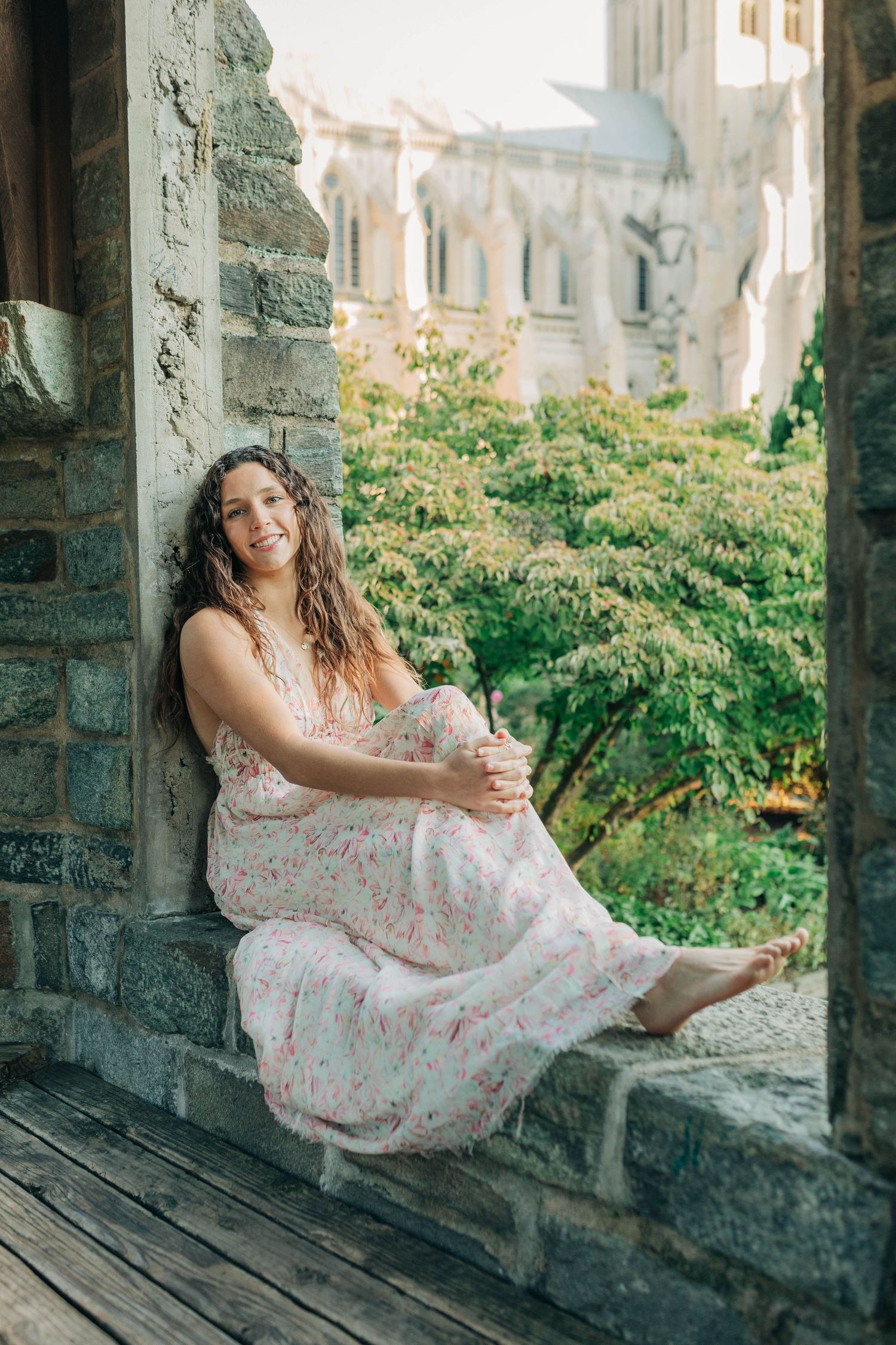 Someone in a floral dress sits casually on a stone windowsill surrounded by architecture.