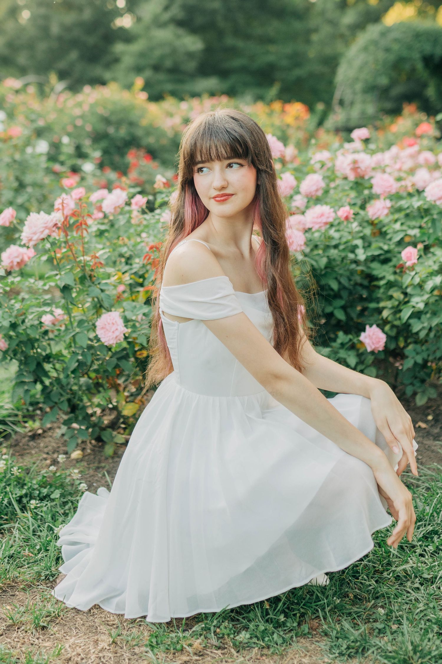 A dreamy summer photoshoot in a rose garden featuring a flowy white dress against lush greenery.