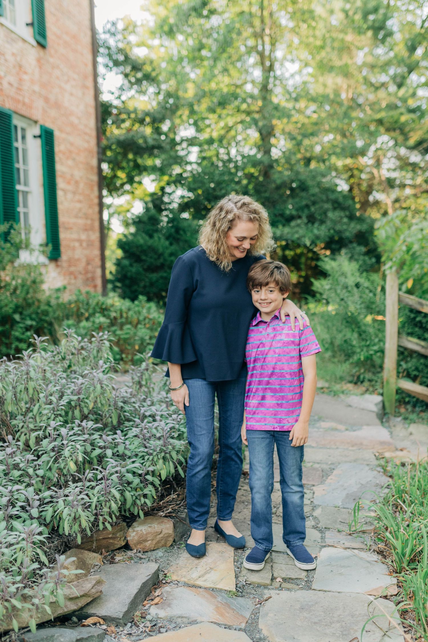 Two people walking together on a stone path surrounded by garden plants.