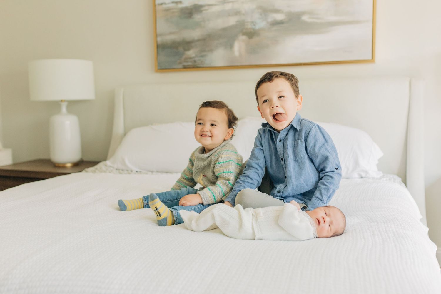 Three siblings in casual attire relax together on crisp white bedding.