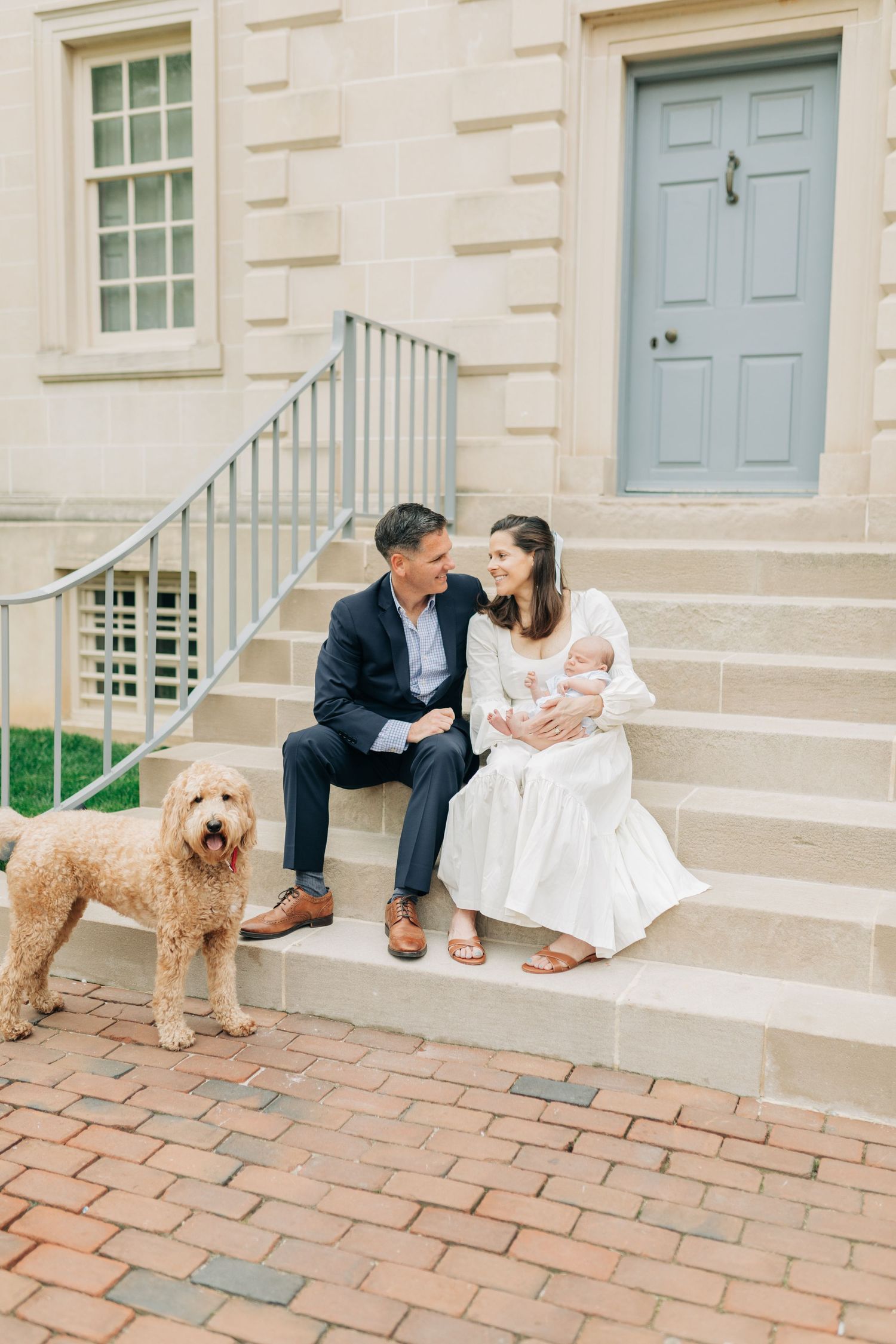 Family and goldendoodle dog relaxing on brick steps of historic building.
