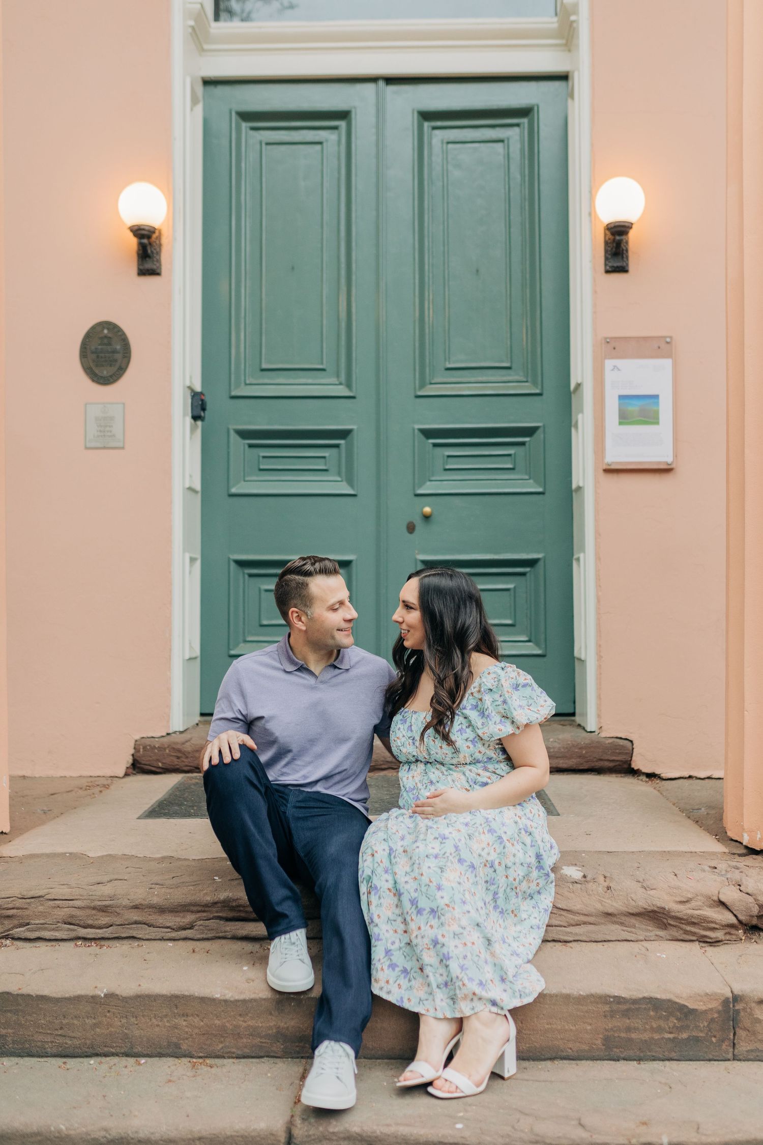 A couple sits and poses together on steps in front of teal colored doors.