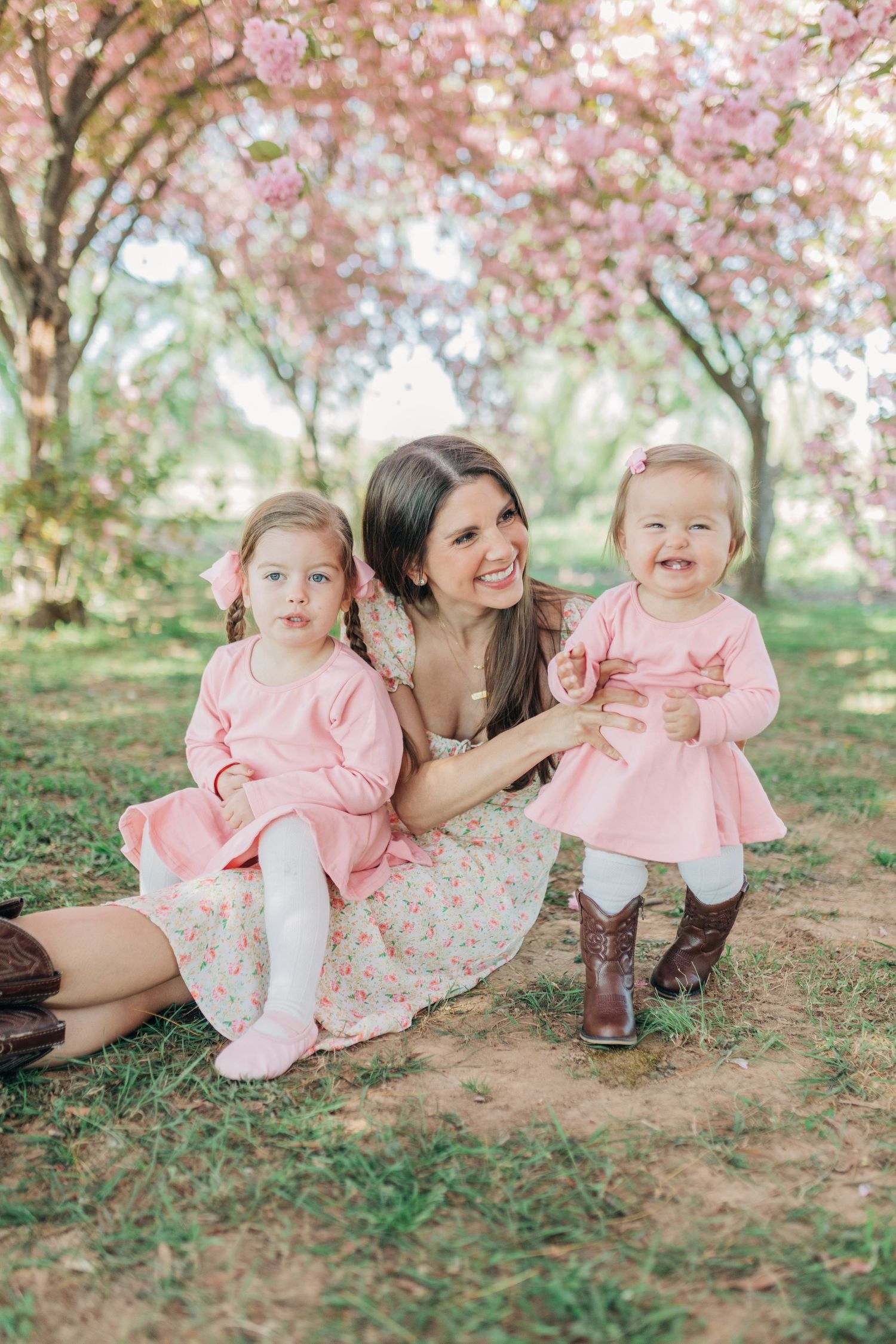 A springtime family portrait under blooming cherry trees with matching pink outfits and brown boots.