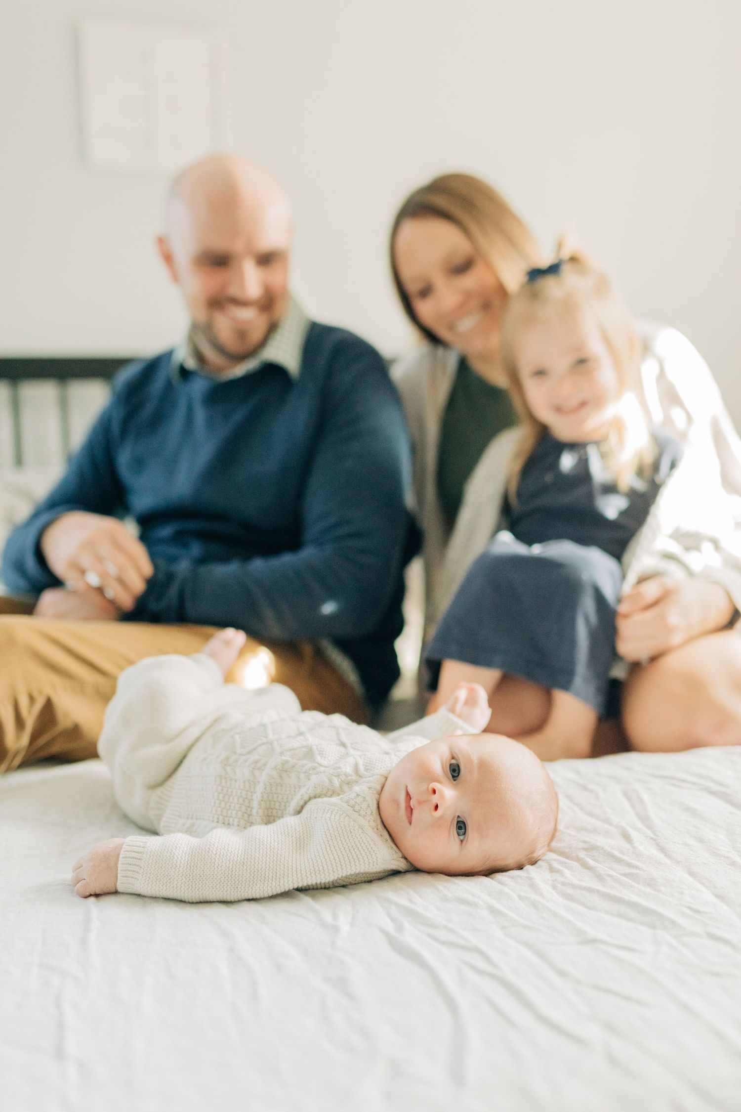 A family relaxes together on a bed while a baby lies contentedly in front.