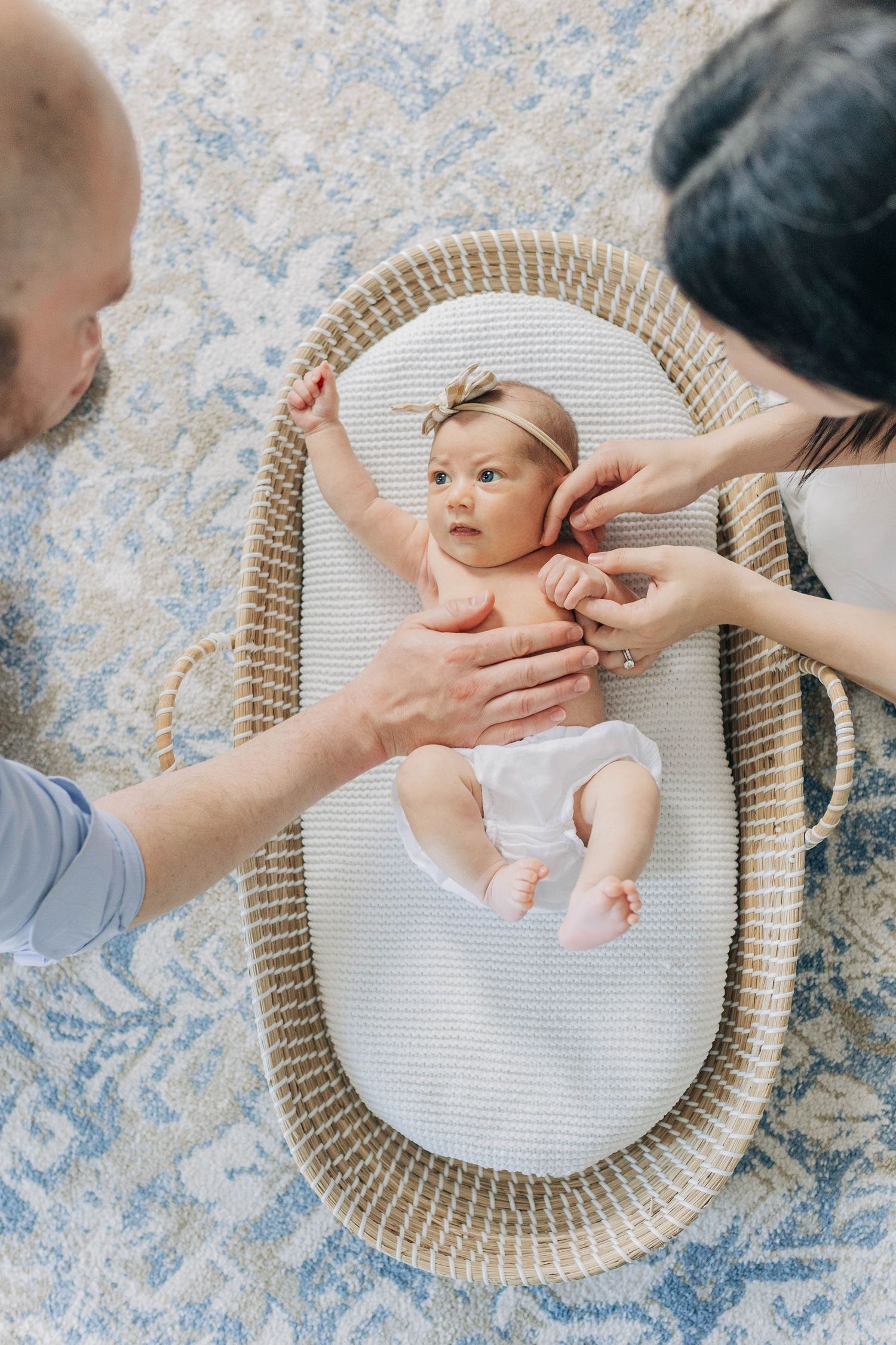 Baby lying in woven bassinet while being gently touched by caring hands.