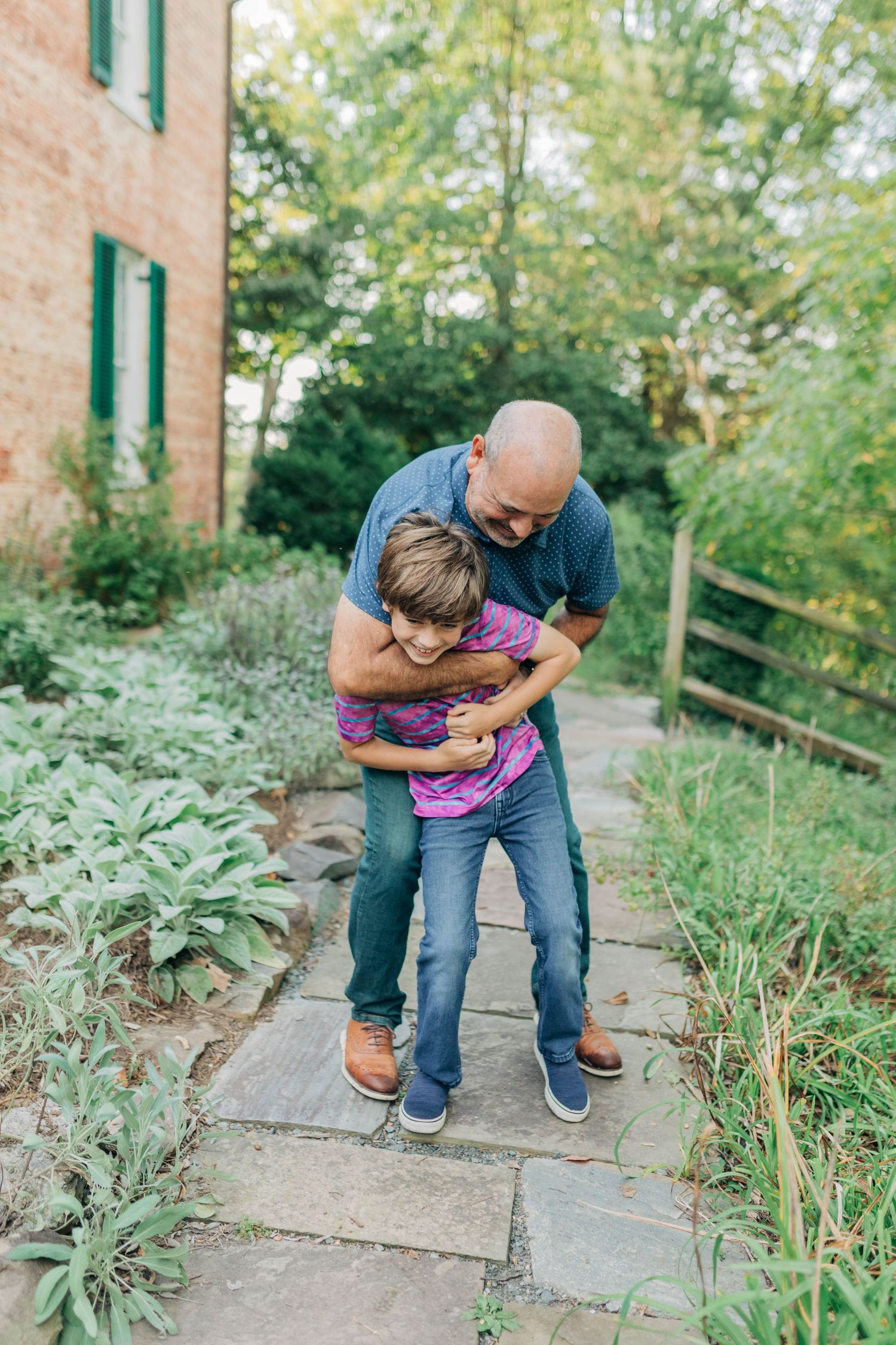 Candid moments captured on stone steps with natural garden surroundings and brick architecture.