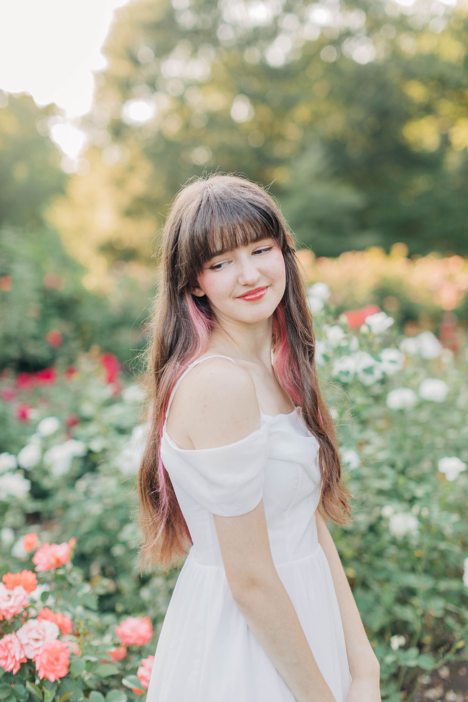 Summer portrait in a rose garden with someone wearing a white off-shoulder dress.