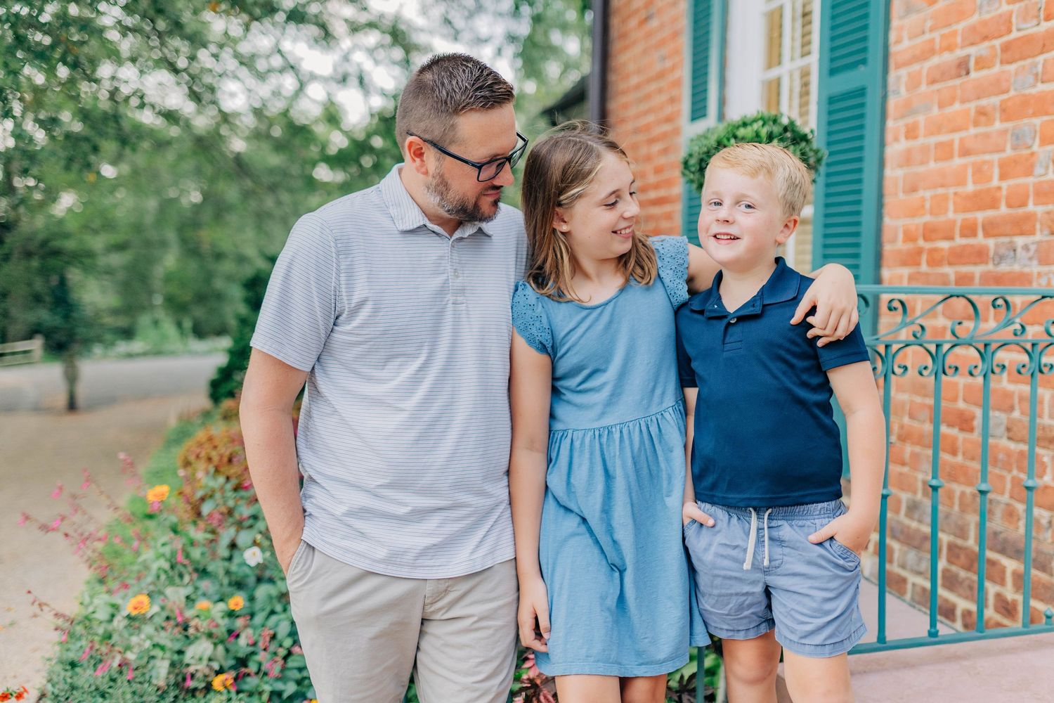 Three people share a candid moment of laughter on brick steps with green shutters in the background.