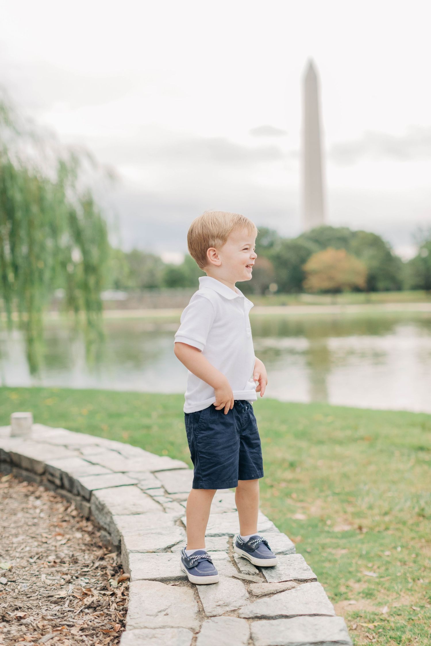 A toddler explores stone steps by a reflecting pool with the Washington Monument in the background.
