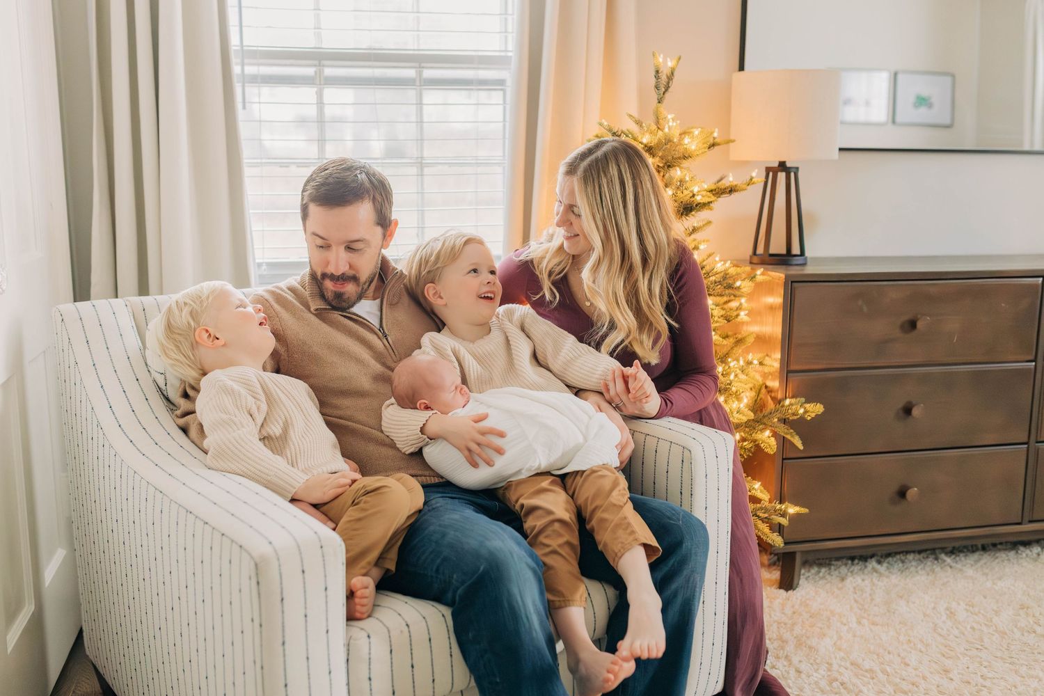A tender family portrait on a white armchair with a decorated Christmas tree in the background.