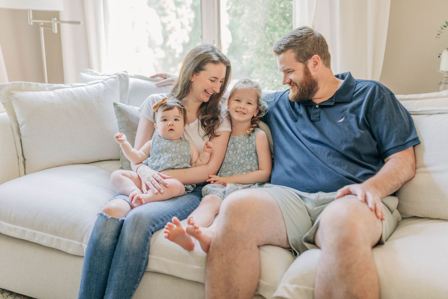 A family shares tender moments together on a comfortable white couch in a bright, airy living room.