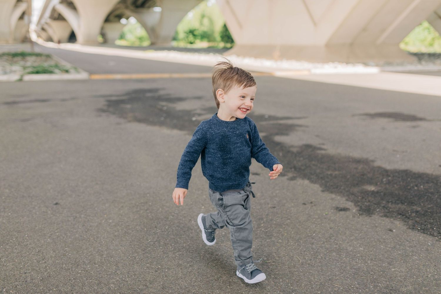 Children running and playing under concrete architectural structure.
