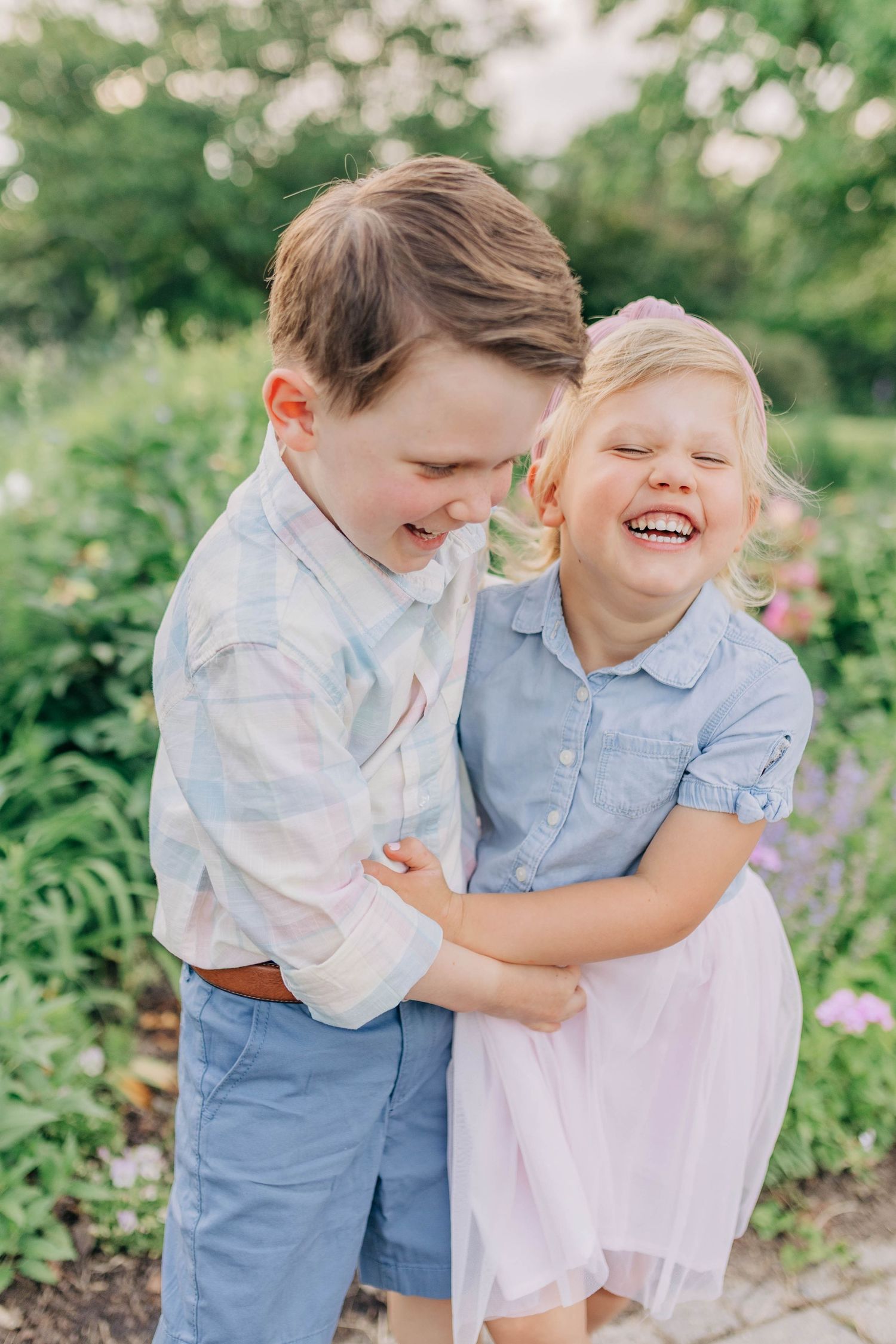 Candid moments of joy between two children embracing and laughing in a garden setting.
